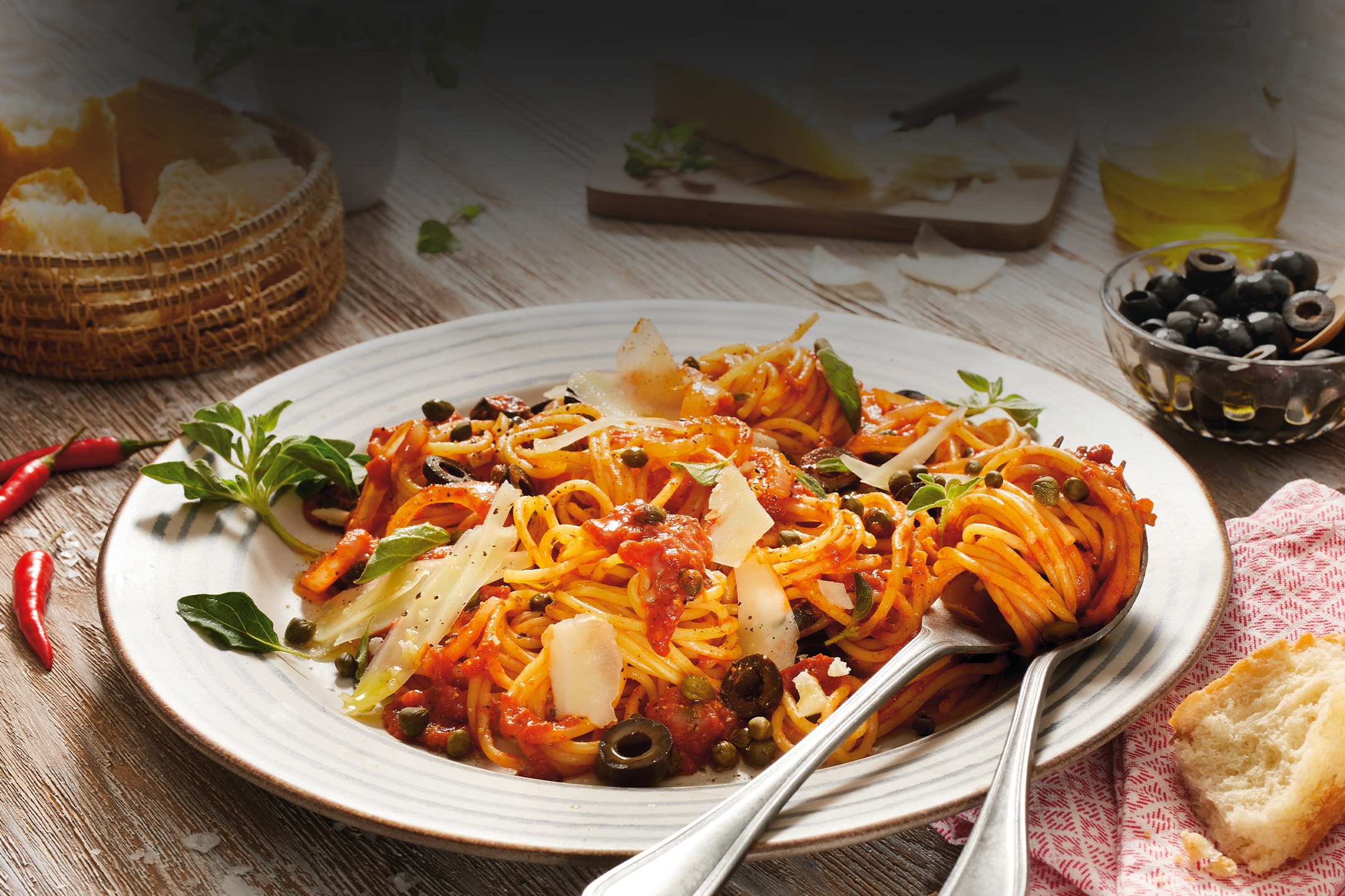 Spaghetti mit Tomatensauce, Oliven, Kapern und Parmesan auf einem Teller.