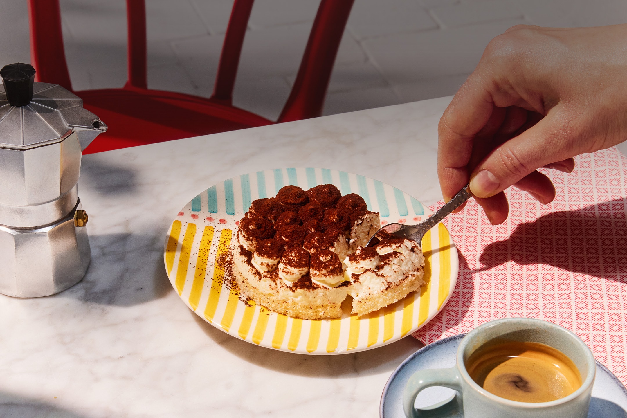 Tiramisù su piatto colorato, caffè e caffettiera su tavolo di marmo.