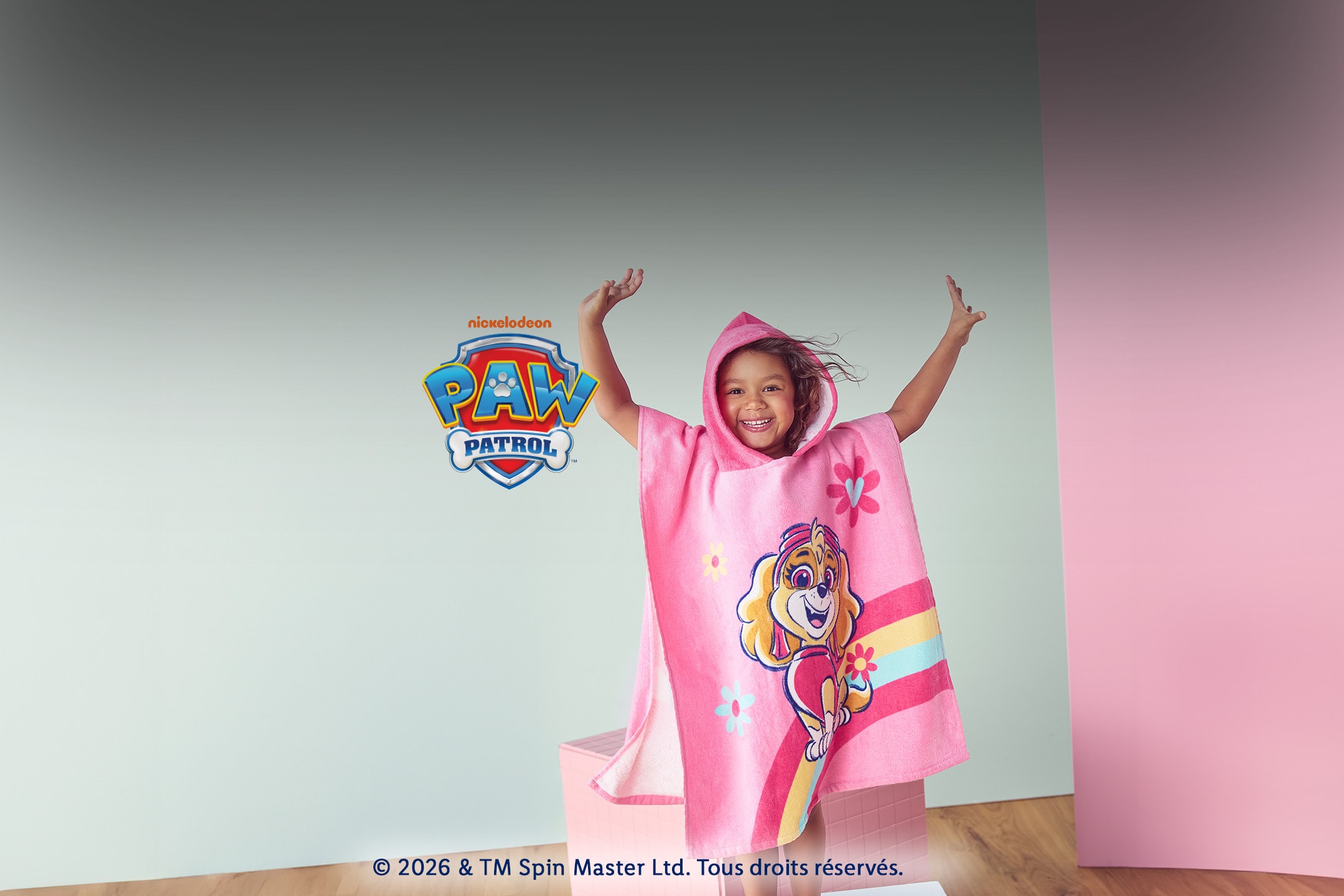 Enfant souriant portant un poncho de bain rose à capuche avec motif Skye et fleurs.