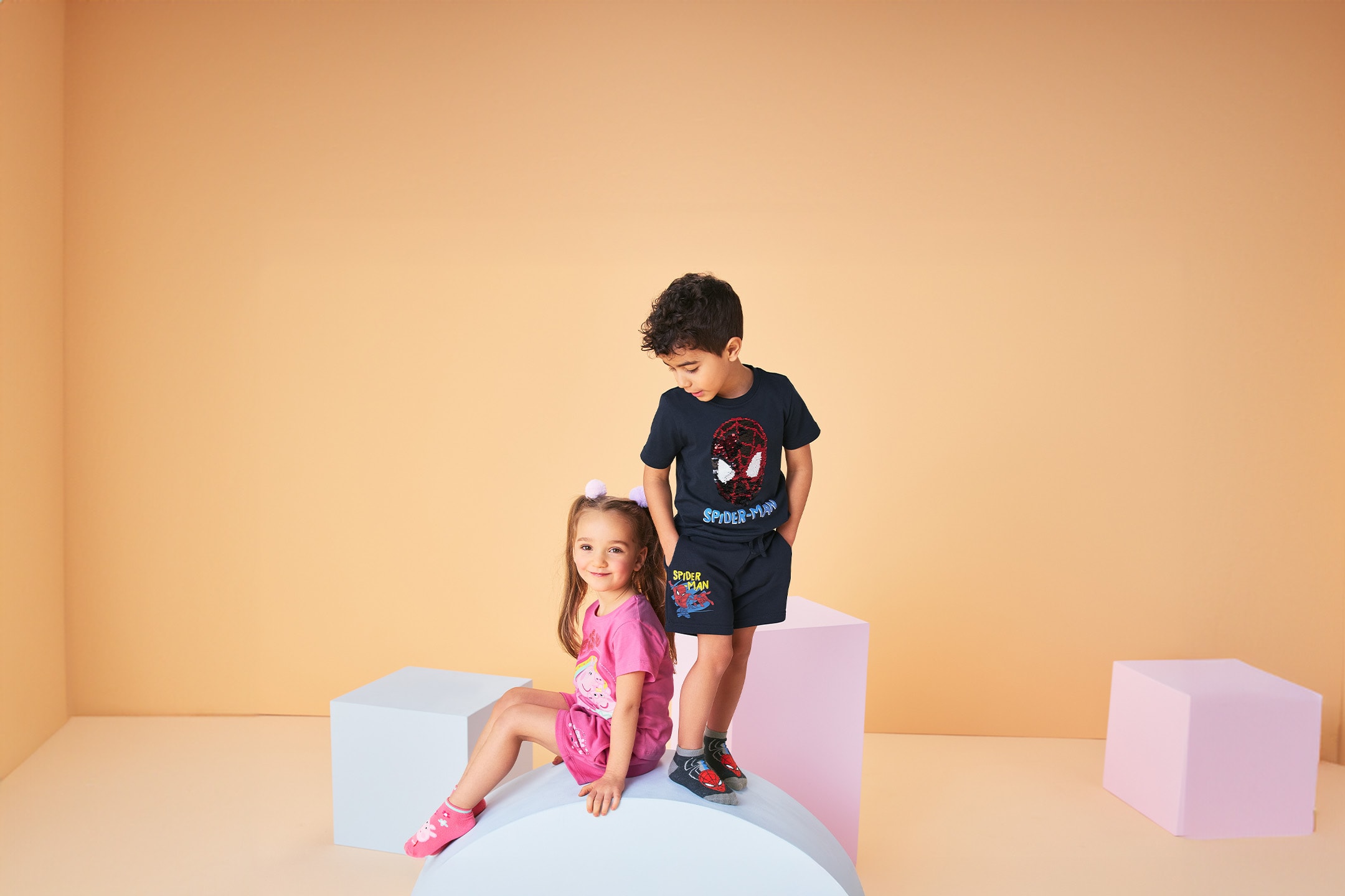 Zwei lächelnde Kinder tragen T-Shirt- und Shorts-Sets mit Superheldenmotiven.