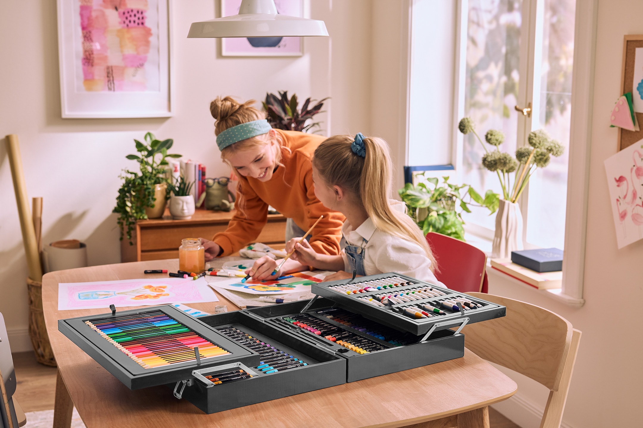 Zwei Kinder malen an einem Tisch mit einem großen Malkasten, inklusive Buntstiften.