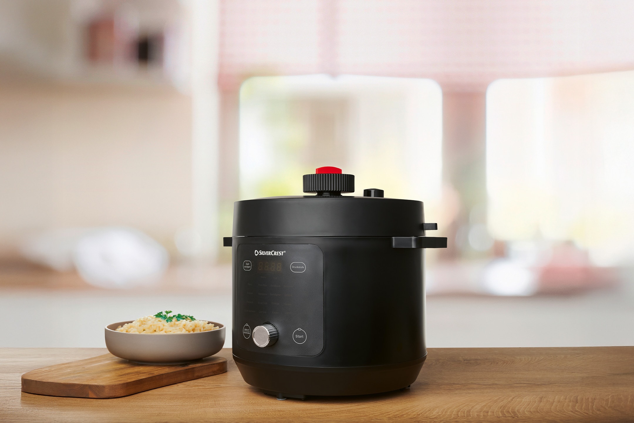 Schwarzer Silvercrest Elektro-Schnellkochtopf mit einer Schale Reis auf einem Schneidebrett.
