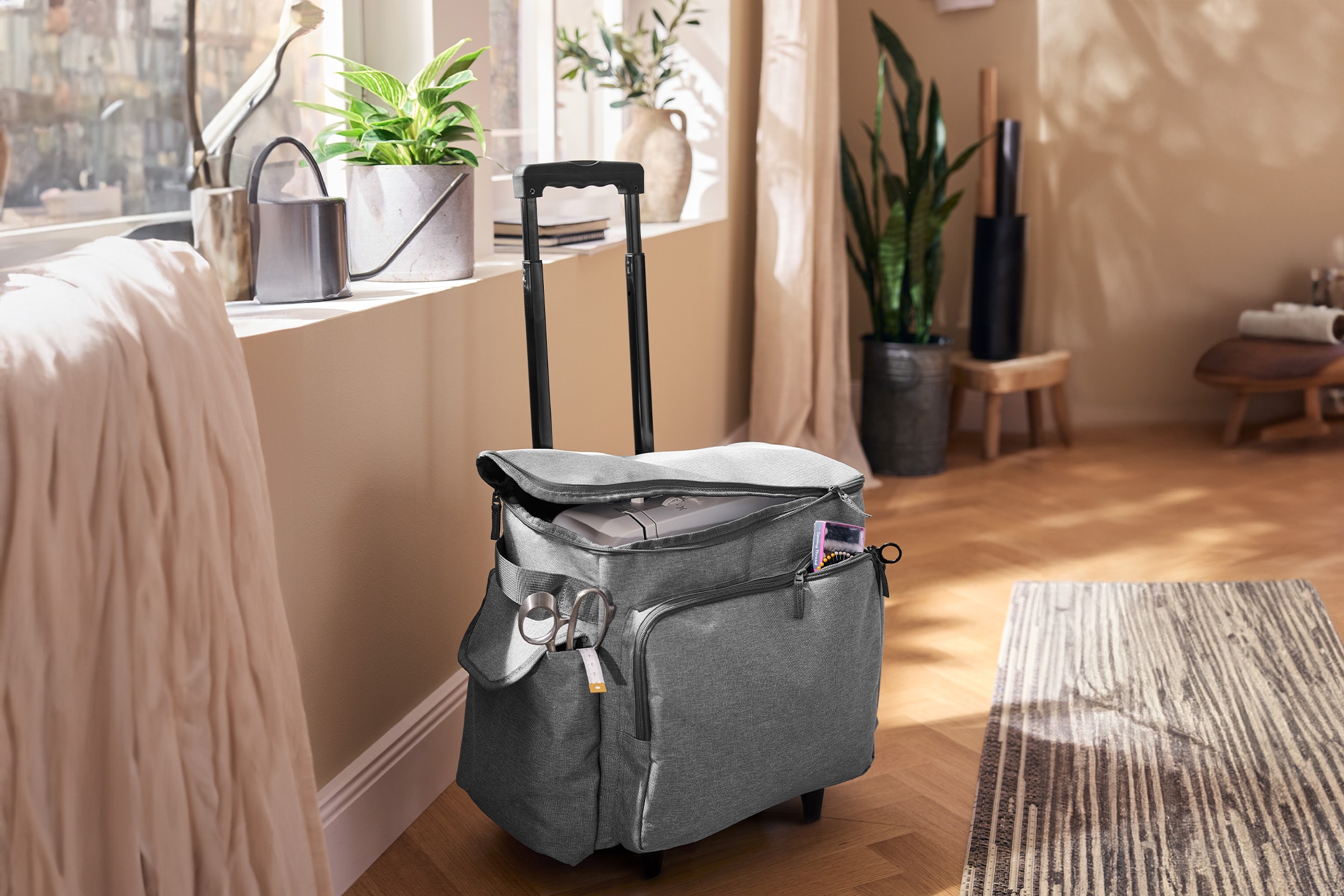 Sac de machine à coudre gris à roulettes avec accessoires de couture dans une pièce lumineuse.