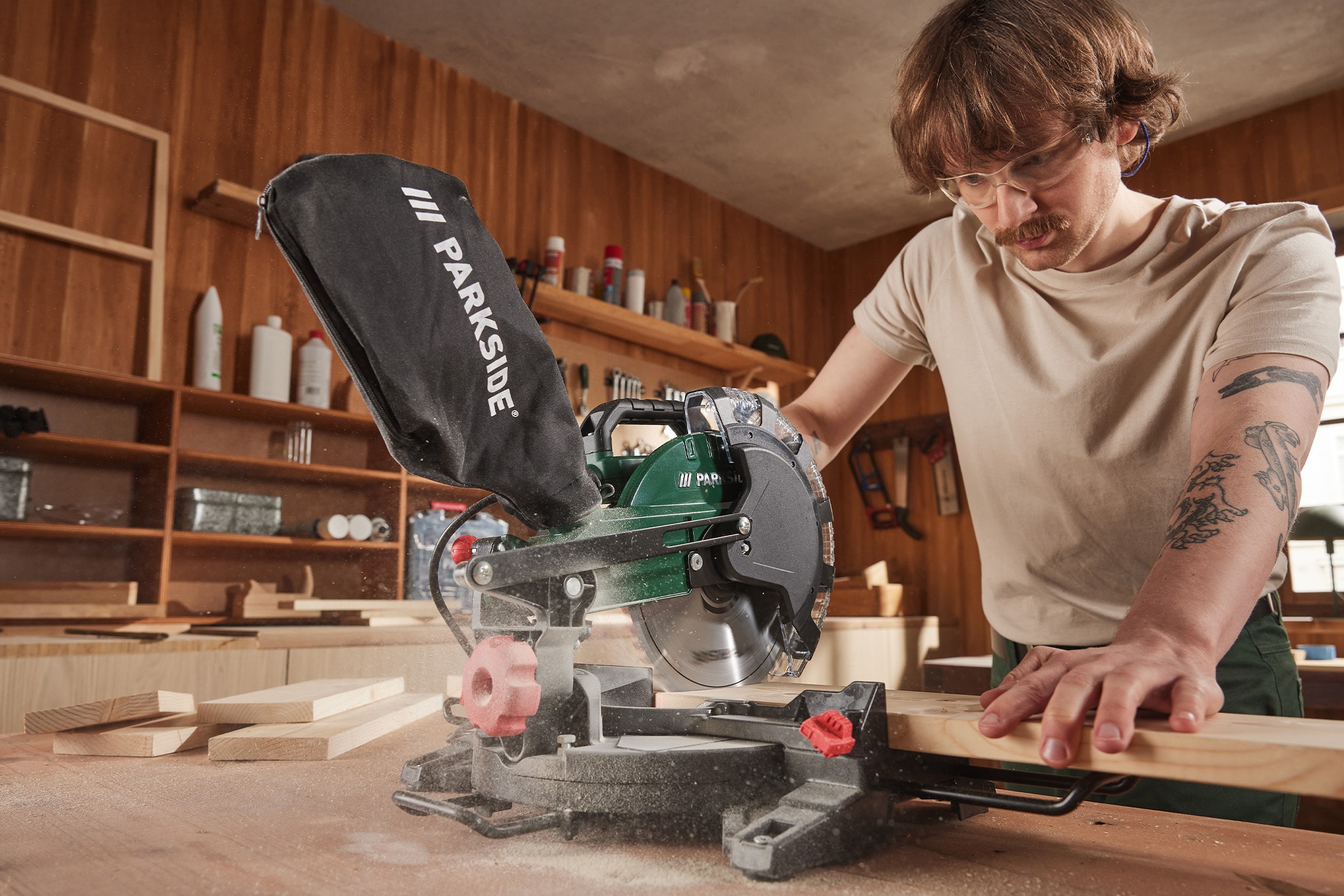 Mann mit Schutzbrille und Parkside Kappsäge, die Holzbretter schneidet.