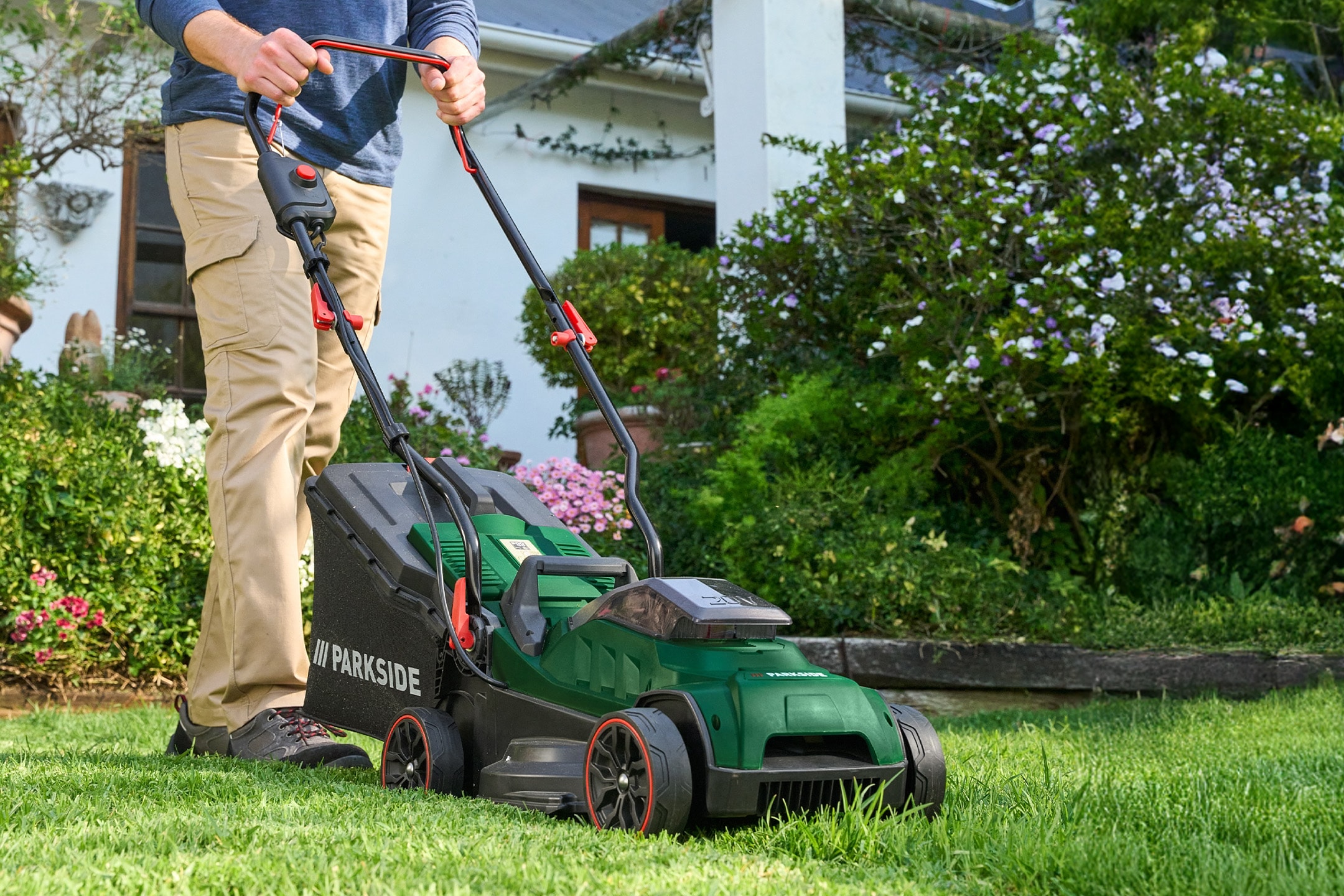 Uomo che taglia il prato con un tosaerba elettrico verde in un giardino soleggiato.