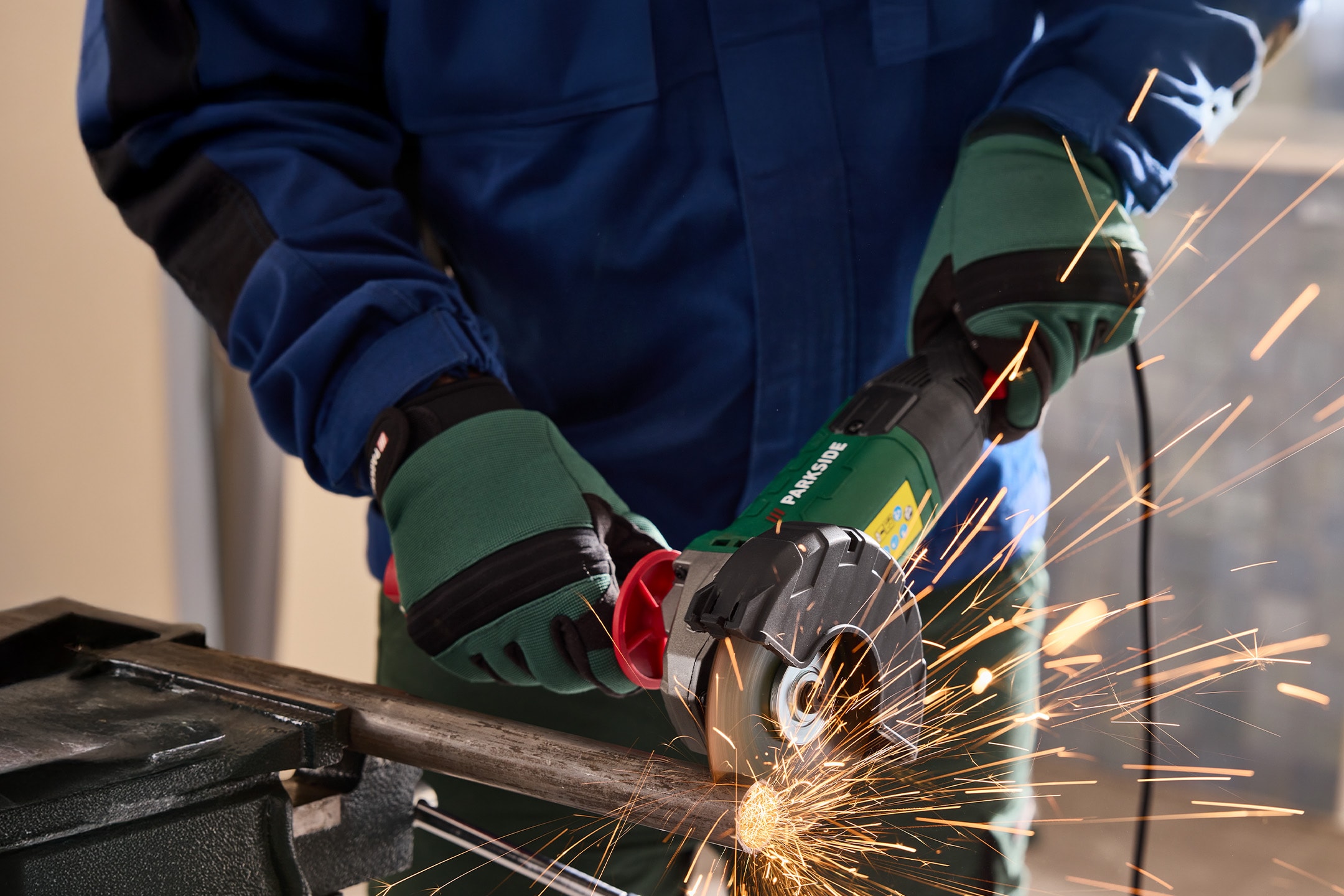 Una persona con guanti da lavoro e tuta, usa una smerigliatrice angolare per tagliare un tubo metallico, producendo scintille.