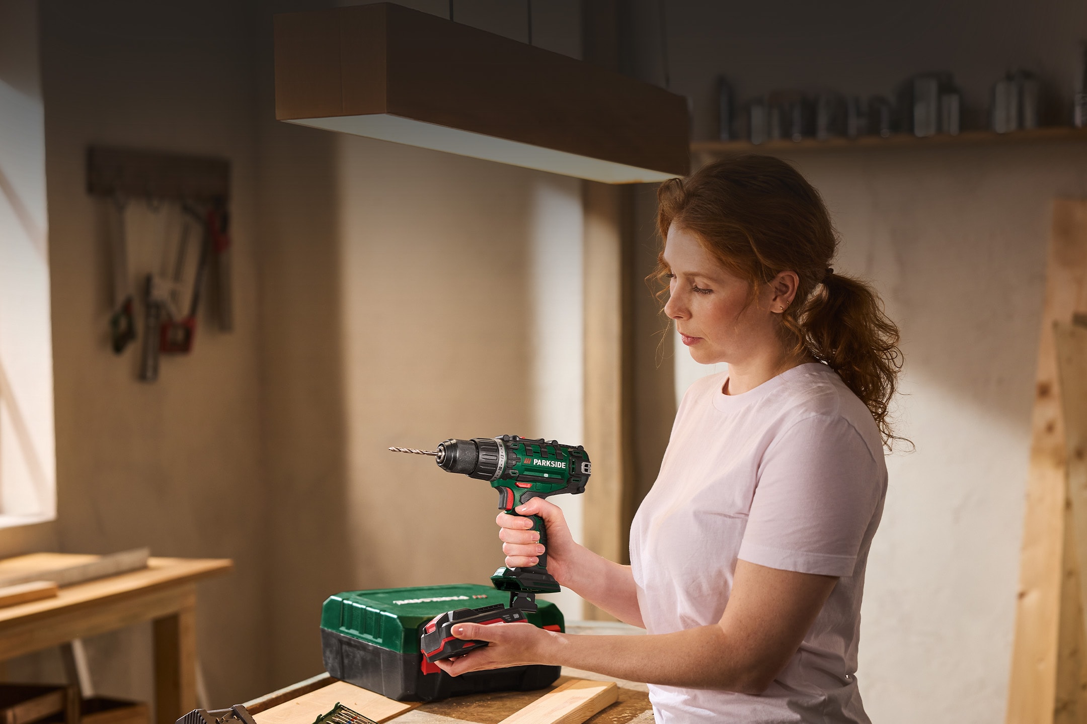 Femme avec perceuse-visseuse sans fil et boîte à outils dans un atelier.