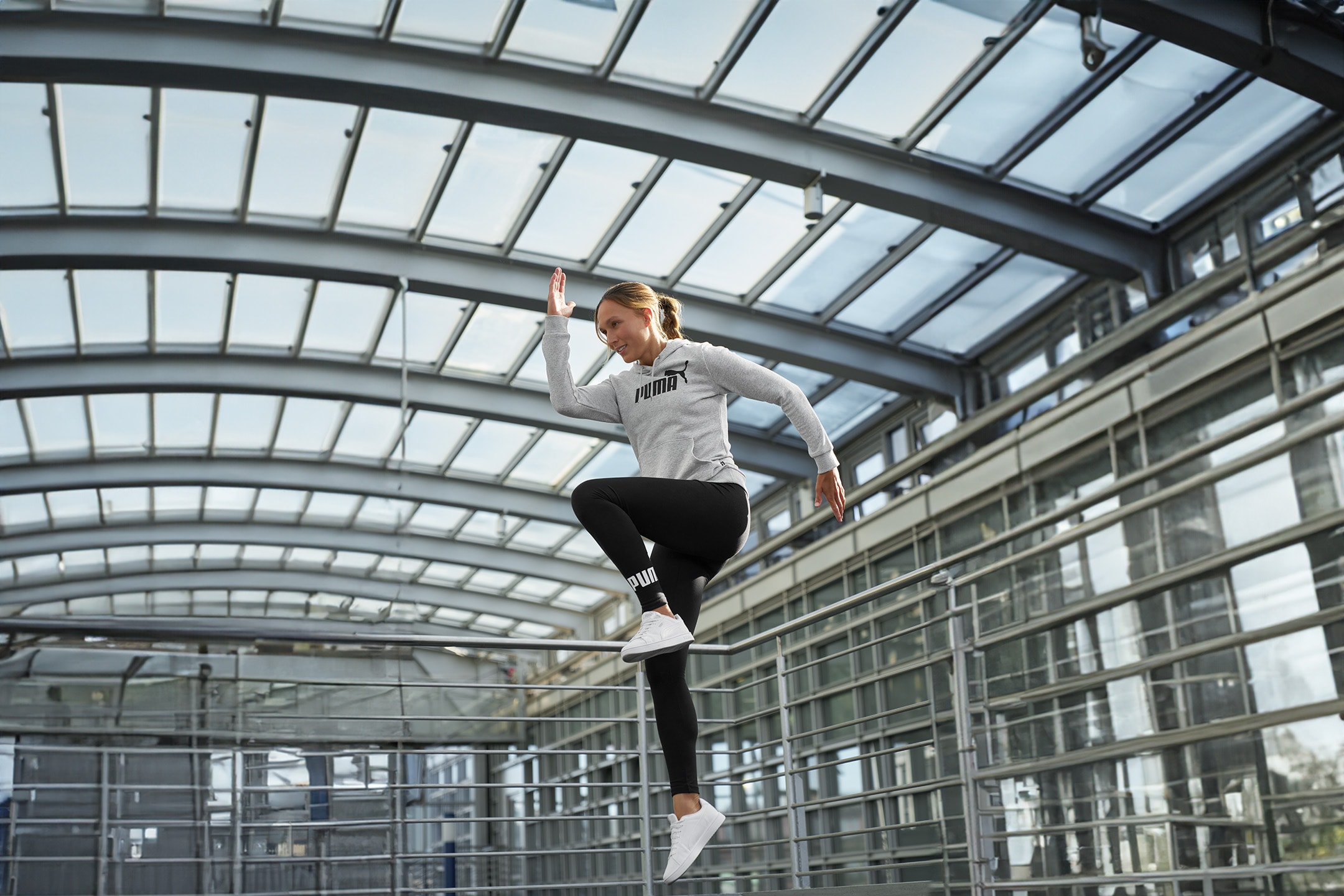 Frau in Sport-Hoodie und schwarzen Leggings springt in einem modernen Gebäude.