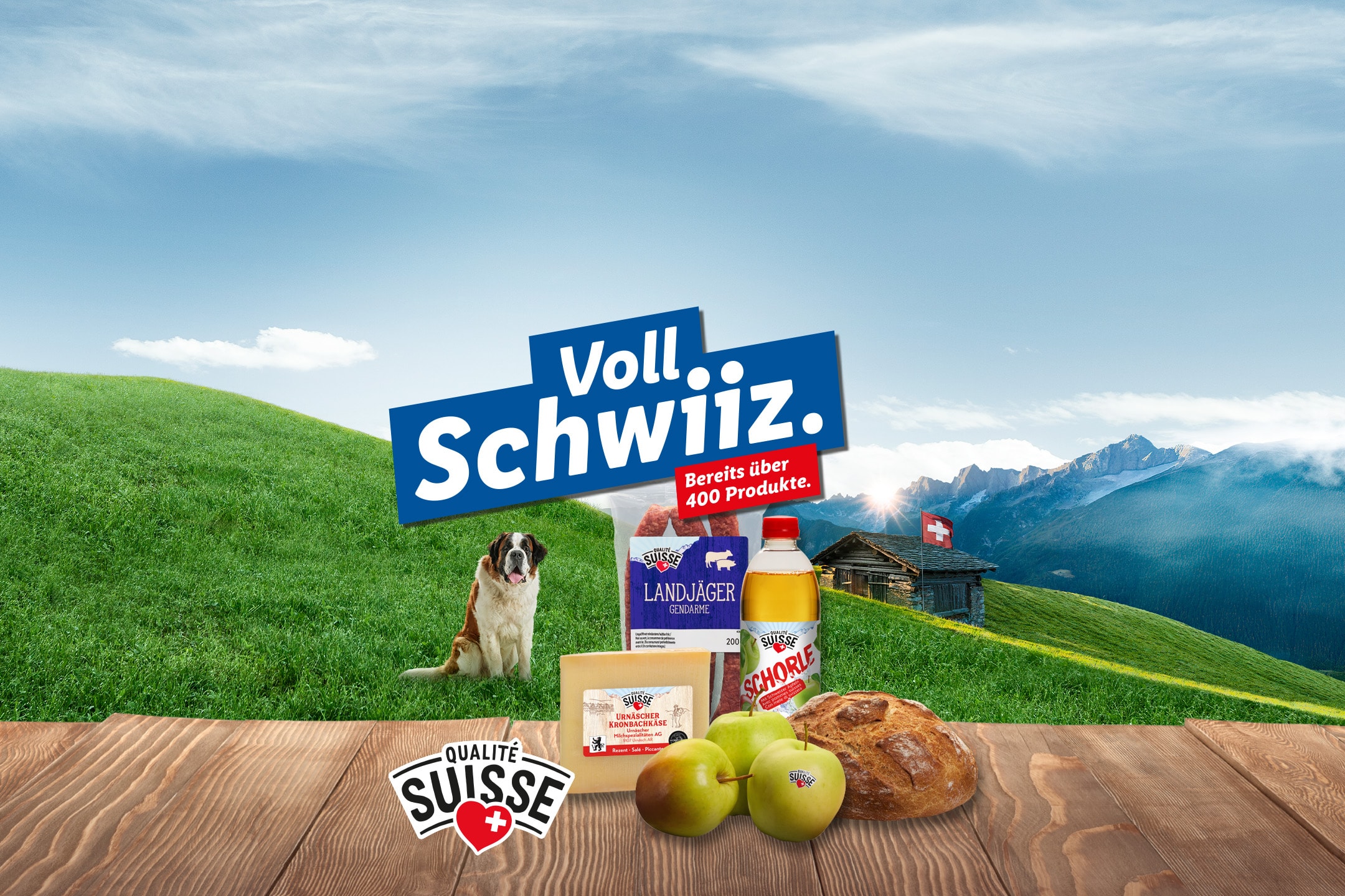 Käse, Äpfel, Brot und Getränke auf einem Holztisch, mit einem Bernhardiner und einer Schweizer Berglandschaft im Hintergrund.