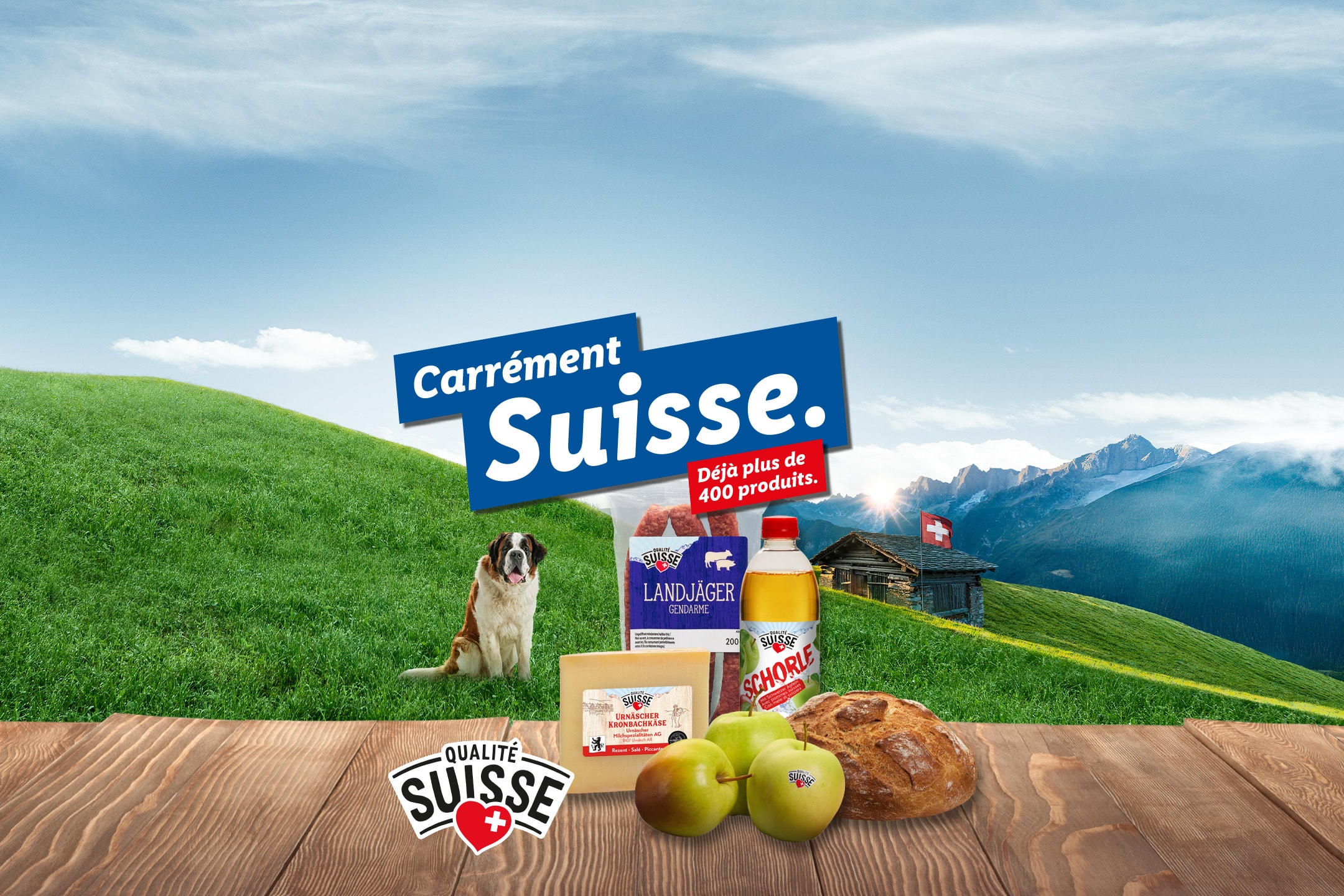 Produits suisses comme fromage, charcuterie, pain, pommes et jus de pomme dans un paysage alpin.