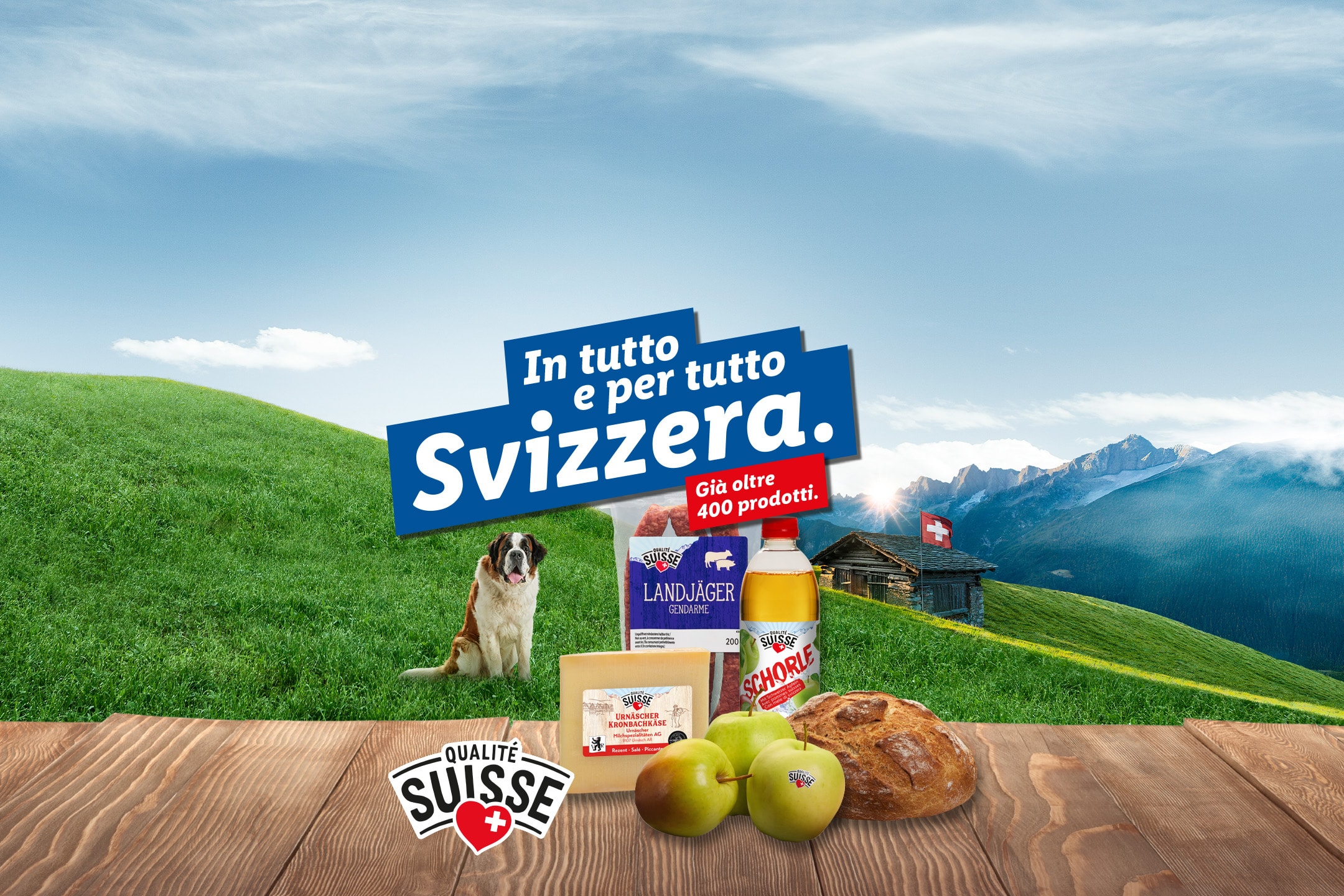 Prodotti svizzeri di qualità come formaggio, salumi, pane e mele su un tavolo di legno, con un paesaggio alpino e un cane San Bernardo sullo sfondo.
