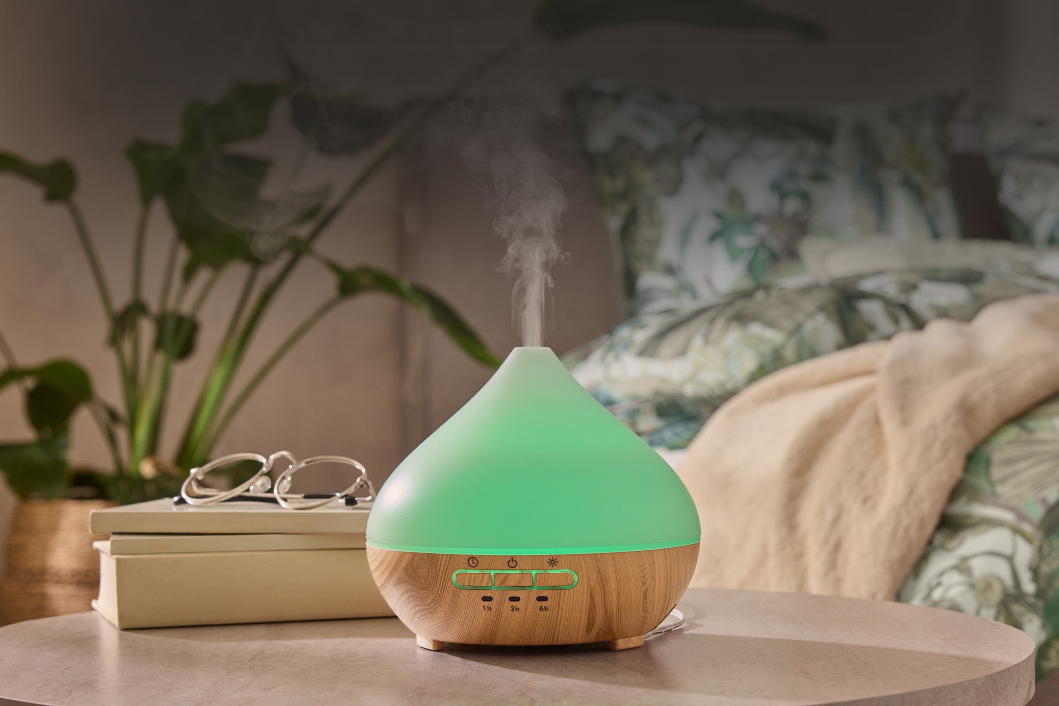 Grüner und hölzerner Aromadiffusor mit Dampf, Brille und Pflanzen in einem Schlafzimmer.
