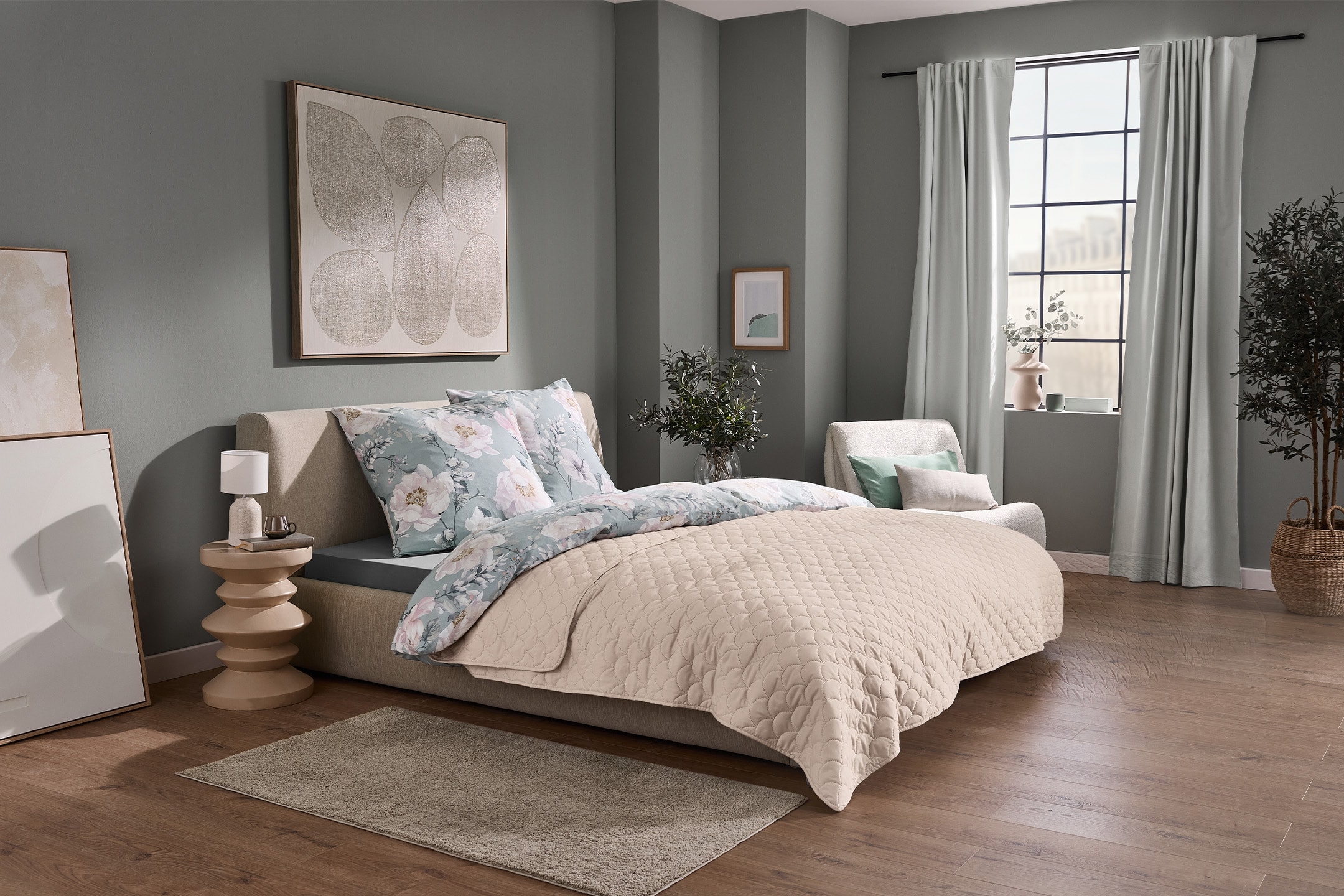 Schlafzimmer mit Bett, floraler Bettwäsche, Steppdecke, Beistelltisch und Fenster.