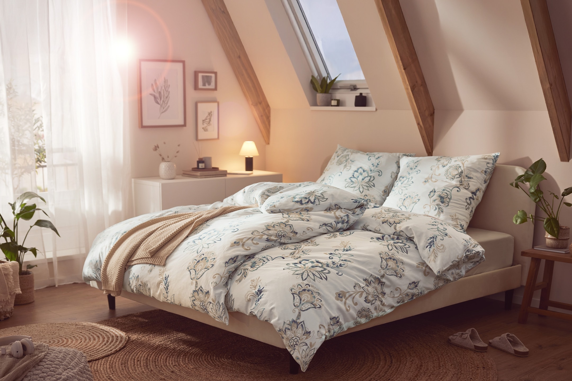 Dachschlafzimmer mit Doppelbett, floraler Bettwäsche, Nachttisch und Pflanzen.