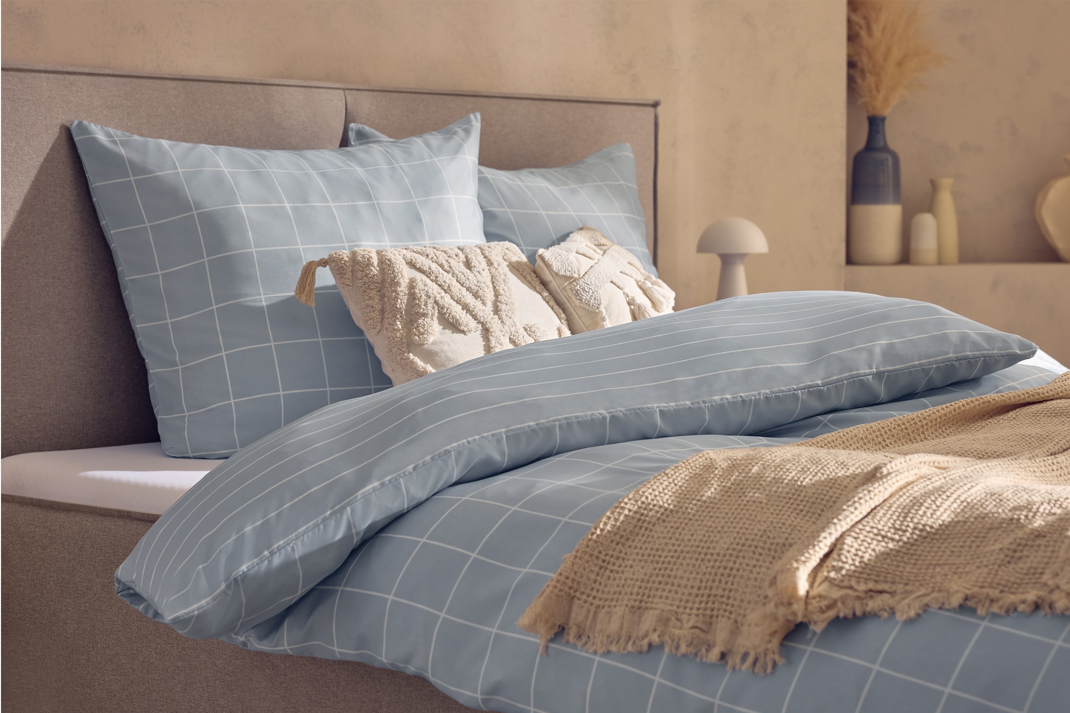 Letto con biancheria da letto azzurra a quadri e cuscini a righe, cuscini decorativi beige e coperta.
