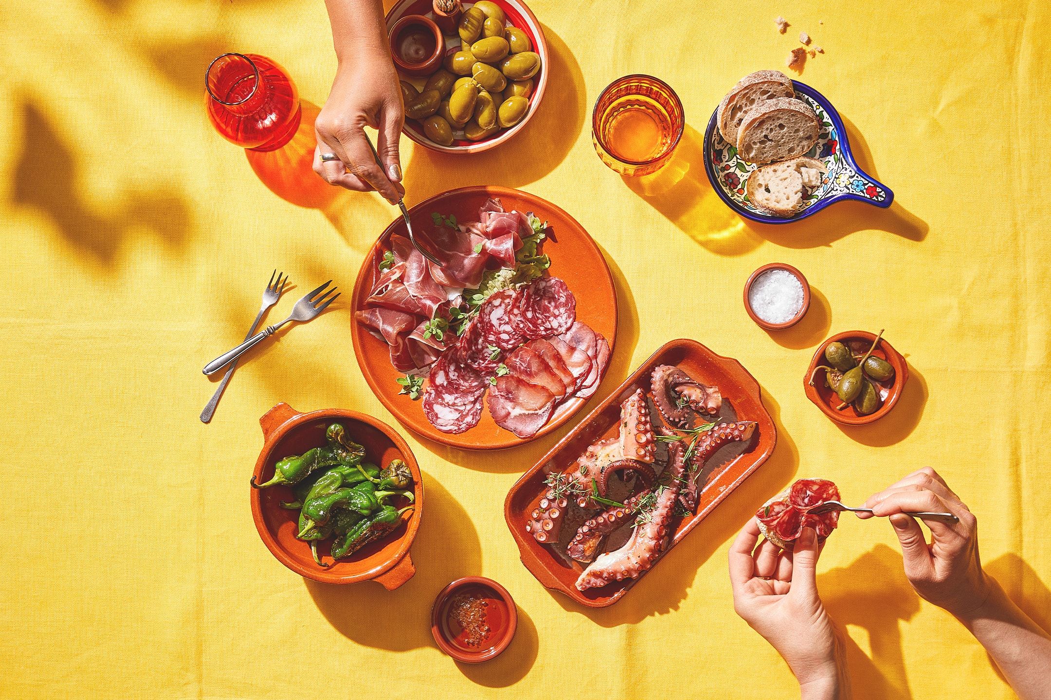 Spanische Tapas mit Oktopus, Wurstwaren, Paprika, Oliven und Brot auf gelbem Tisch.