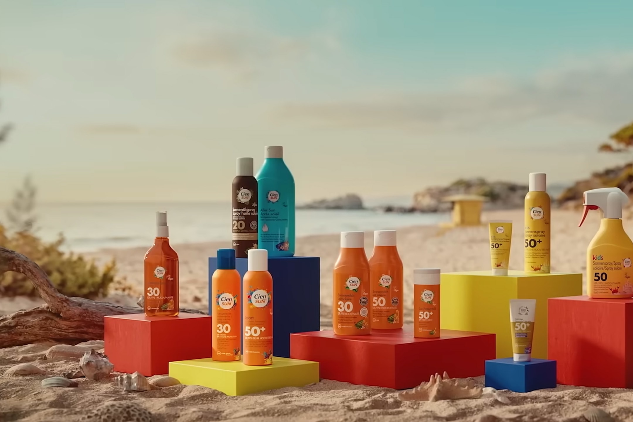 Eine Auswahl an Sonnenpflegeprodukten, darunter Sprays und Lotionen, an einem sonnigen Strand.
