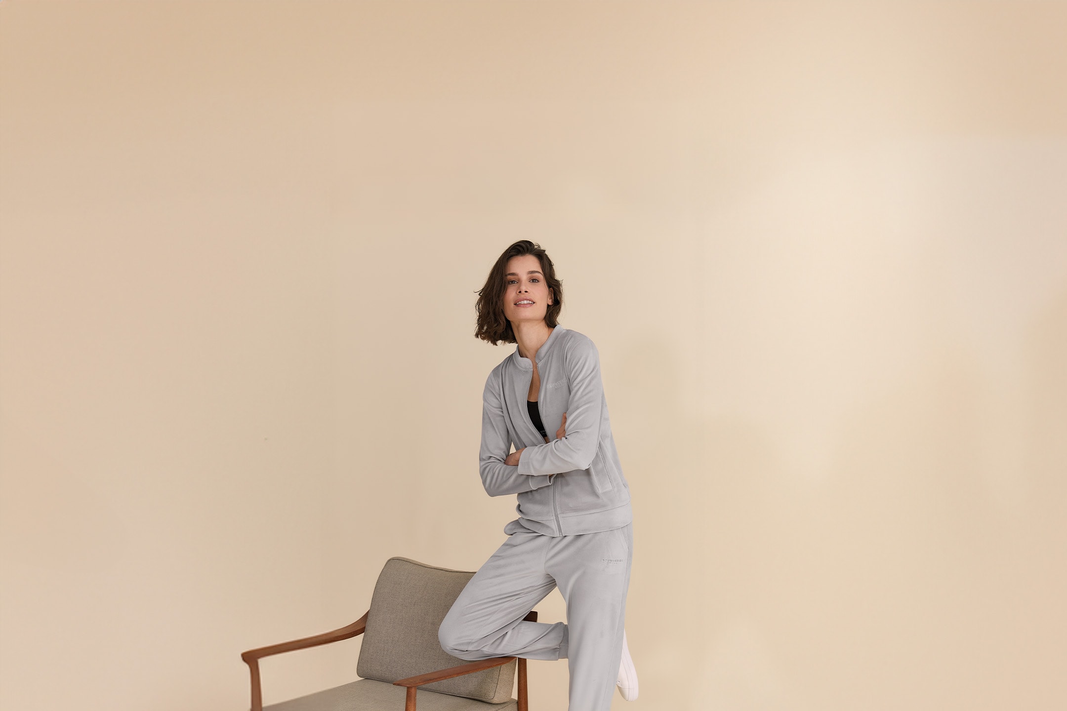Frau in grauem Trainingsanzug und schwarzem Sport-BH, lächelnd, auf einem Stuhl lehnend