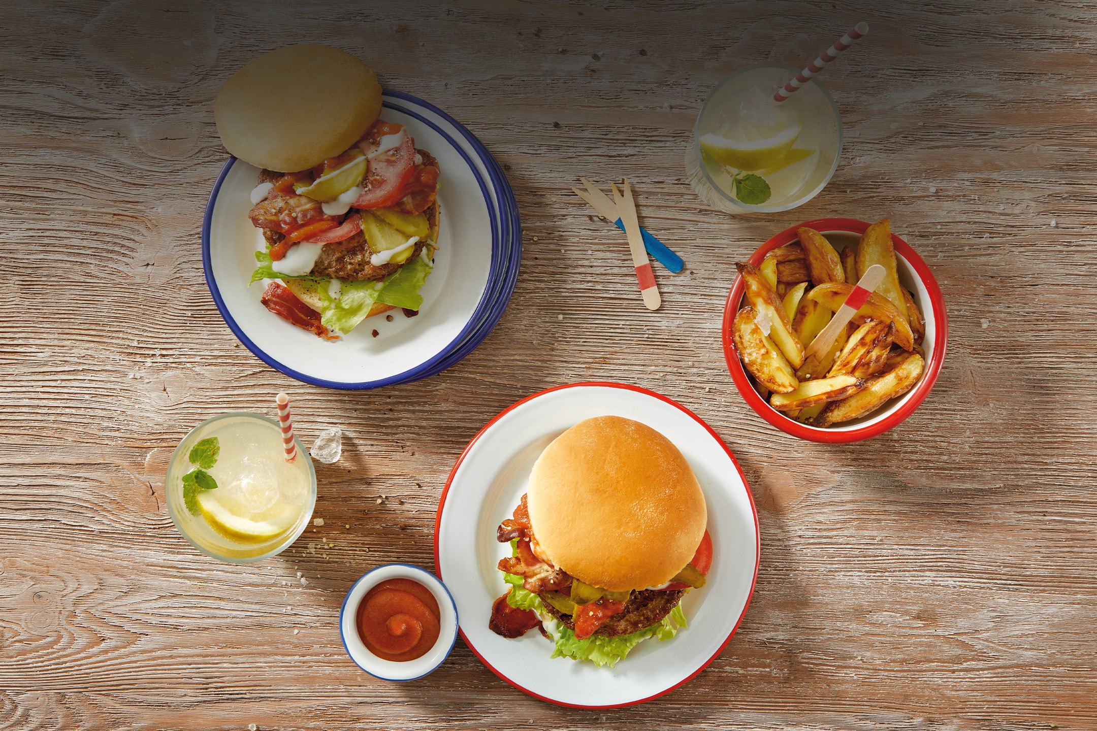 Deux hamburgers avec frites et boissons rafraîchissantes sur une table en bois.