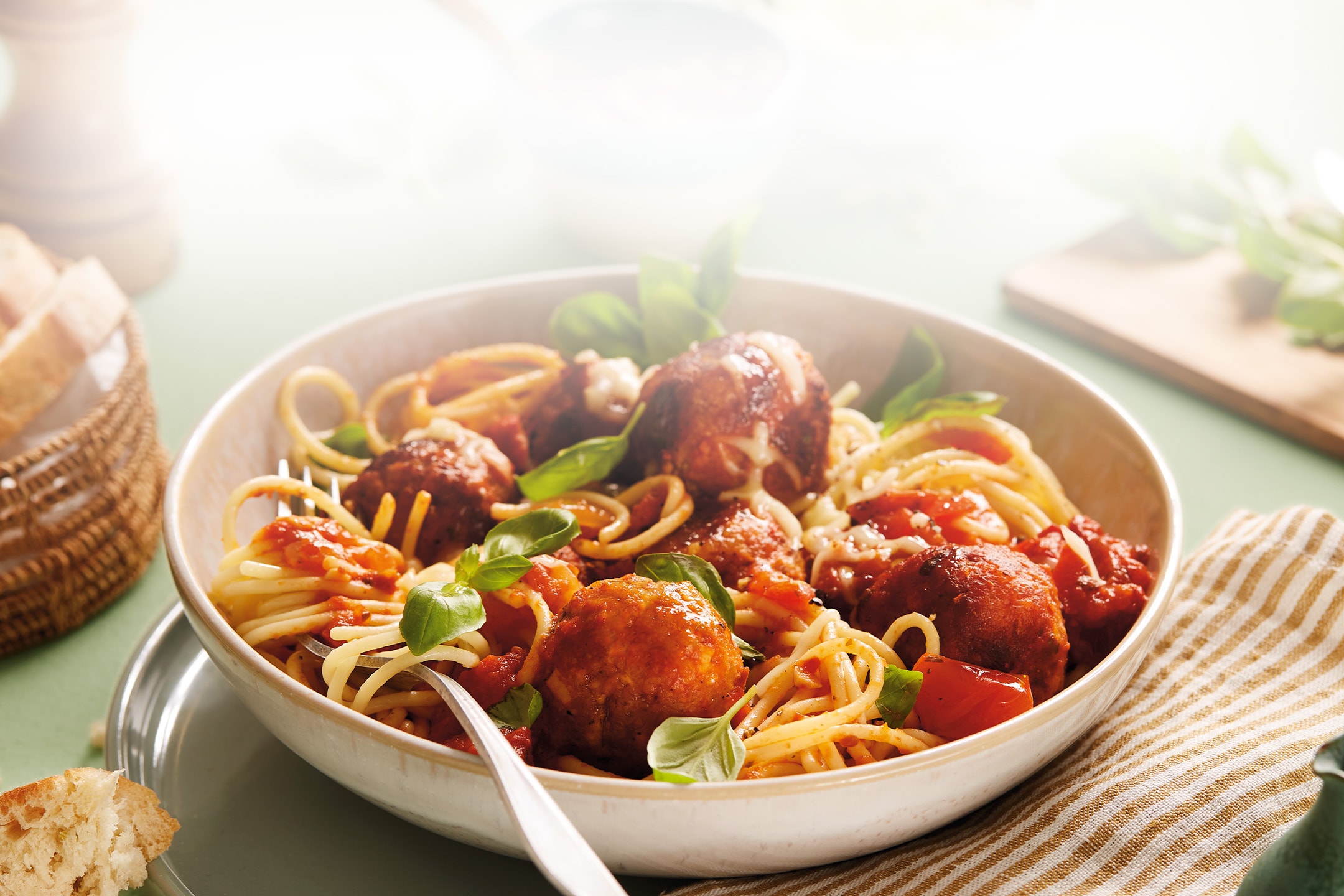 Spaghetti mit Fleischbällchen, Tomatensauce und frischem Basilikum in einer Schüssel, mit Brot daneben.