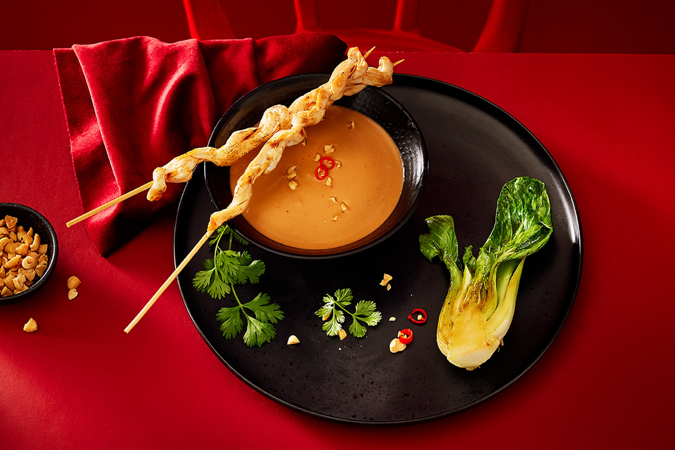 Brochettes de poulet avec sauce aux cacahuètes, pak choï et coriandre sur une assiette noire