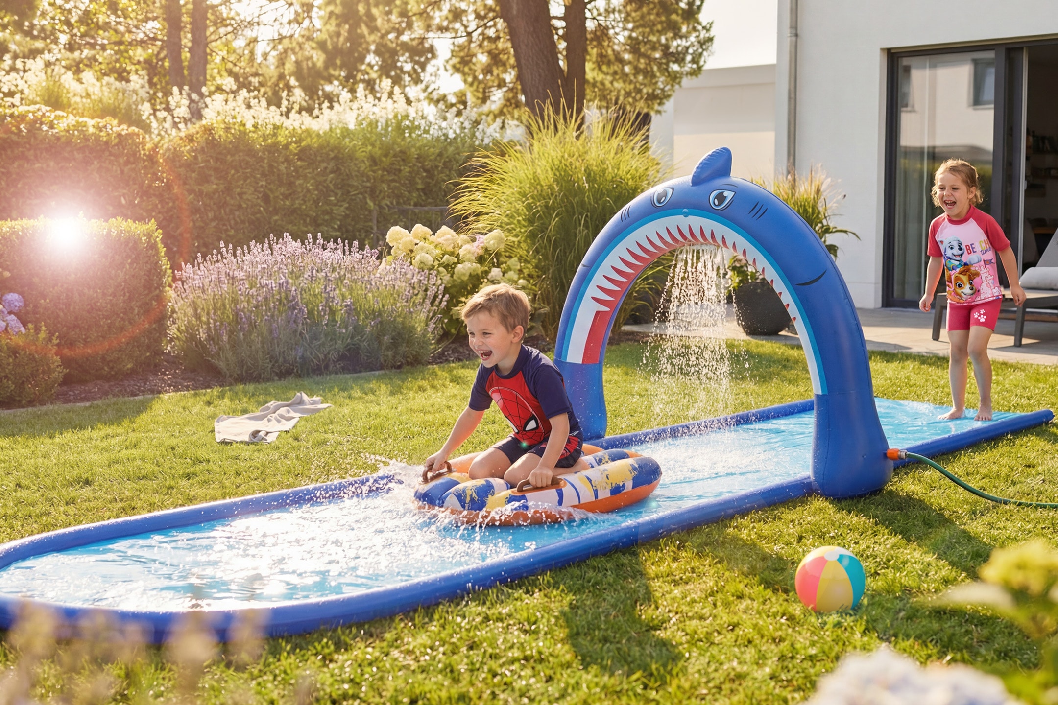 Zwei Kinder spielen mit einer Haifisch-Wasserrutsche in einem sonnigen Garten.