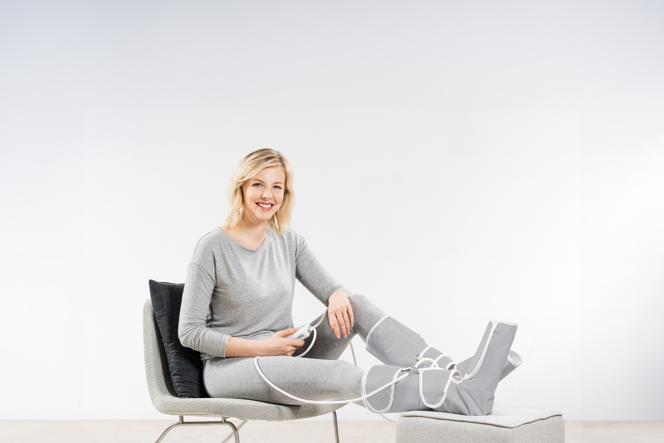 Donna sorridente con massaggiatore per gambe a compressione, seduta su una sedia.