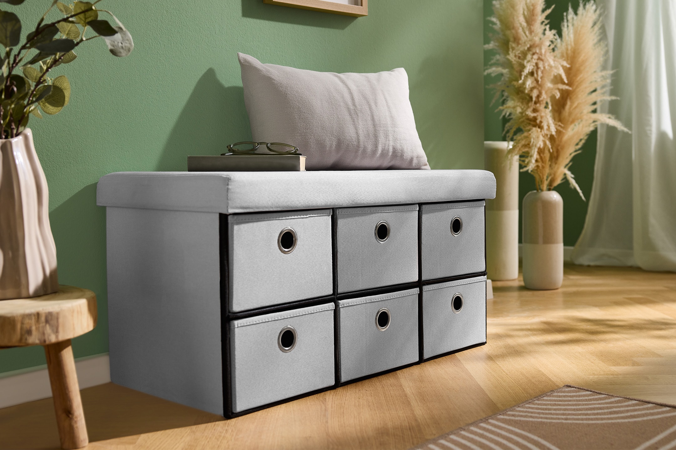 Graue Aufbewahrungsbank mit sechs Stoffschubladen, Kissen und Pflanzendekoration.