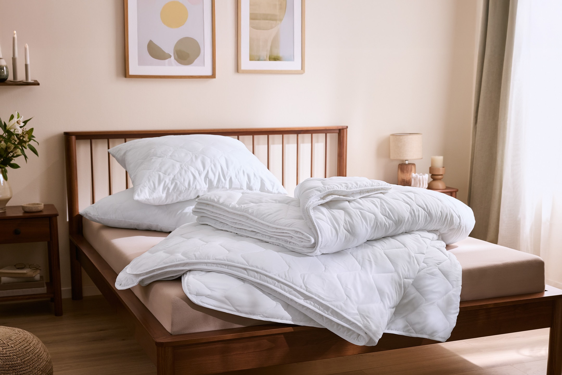 Weiße gesteppte Bettdecken und Kissen auf einem Holzbett in einem hellen Schlafzimmer.