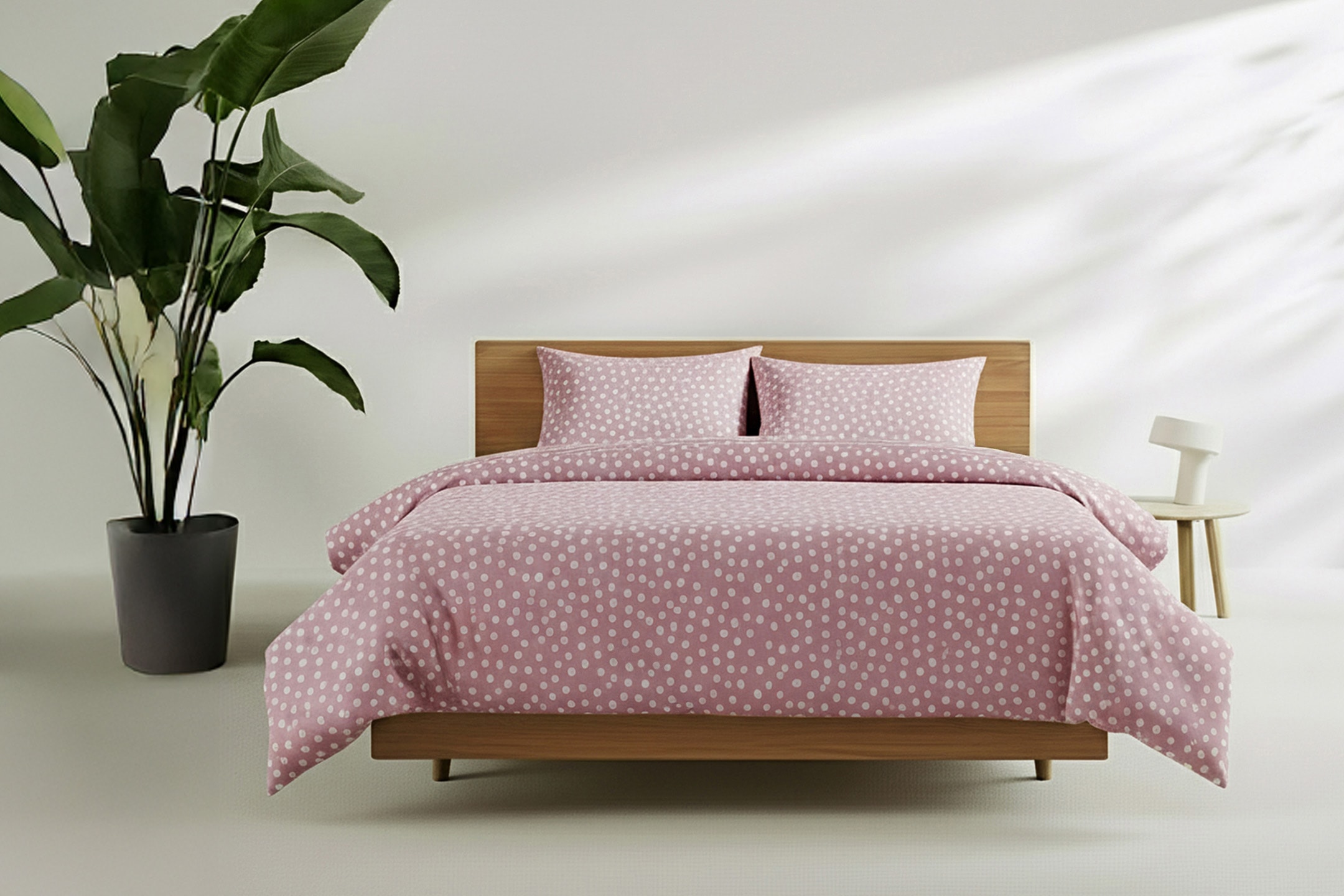 Letto con lenzuola rosa a pois bianchi, pianta verde e comodino con lampada.