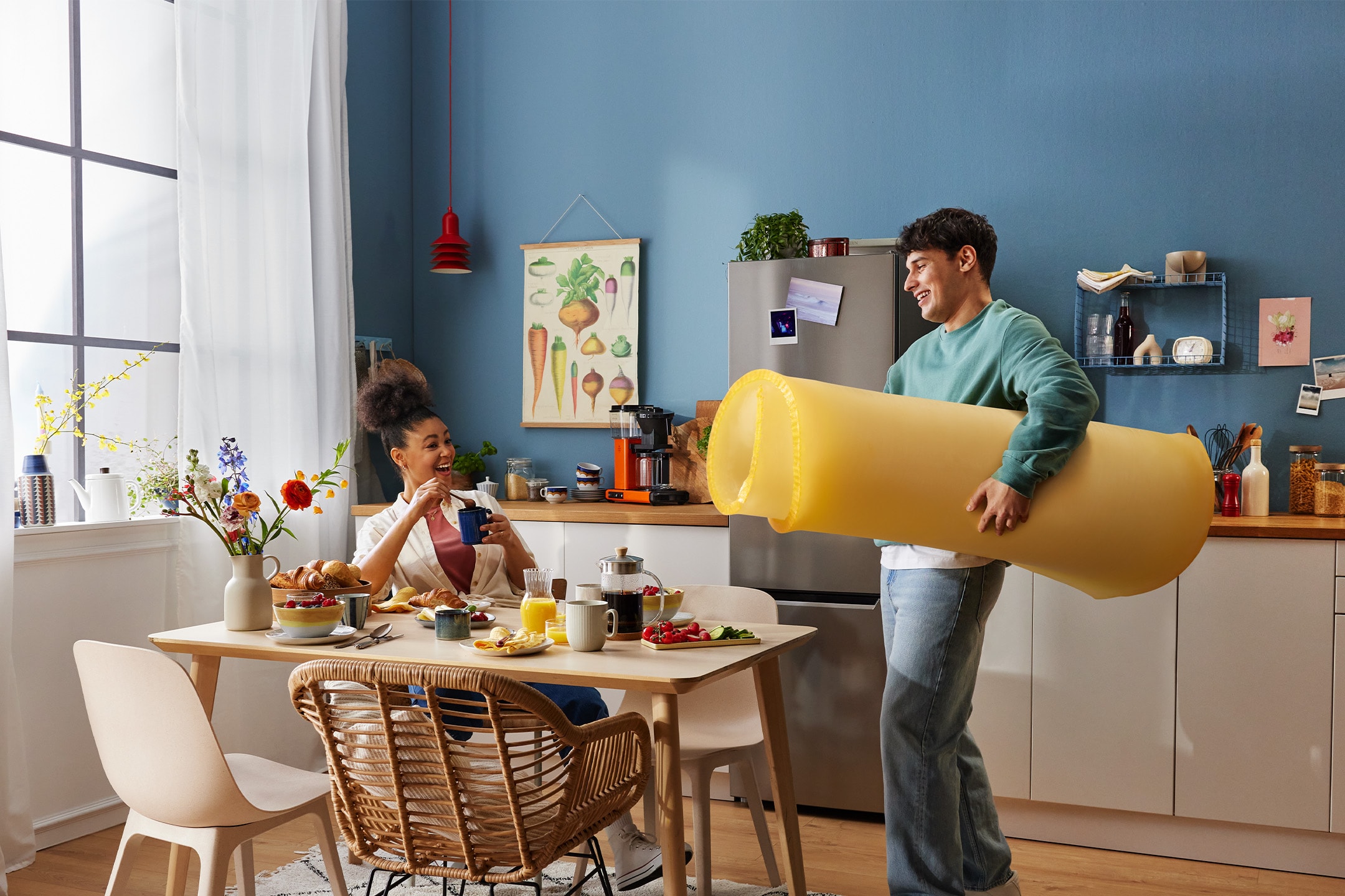 Ein Paar frühstückt in der Küche, der Mann hält eine riesige Nudelrolle.