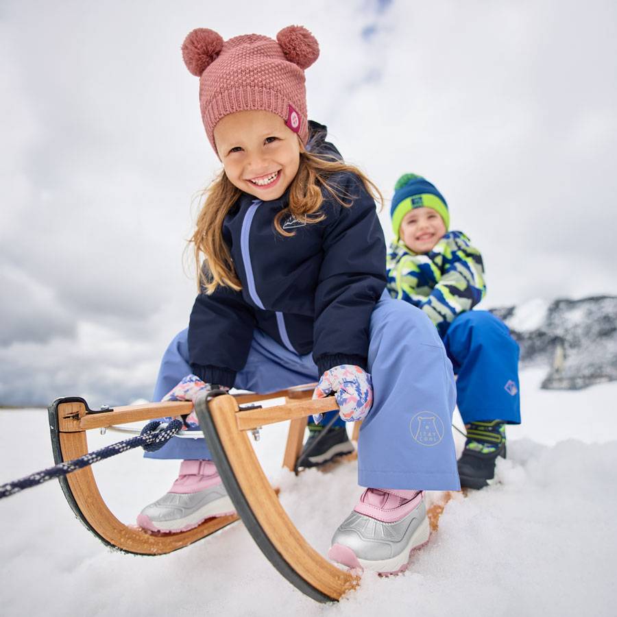 Bambini con abiti invernali e cappelli con pon-pon, che slittano sulla neve.