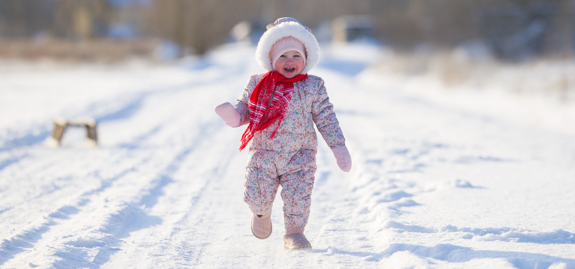 Bambina gioiosa in tuta invernale e sciarpa che corre su un sentiero innevato.