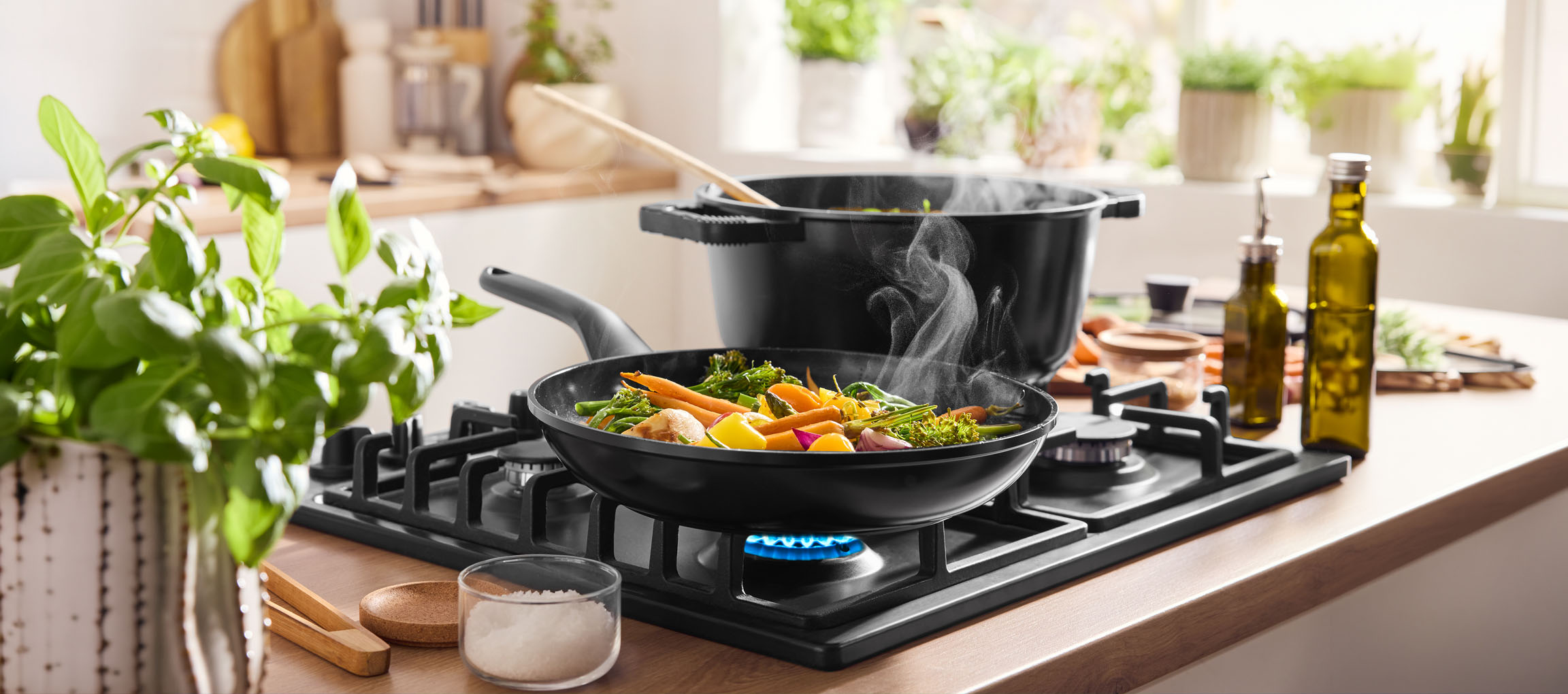 Gemüse in einer Pfanne auf einem Gasherd kochen, mit Topf und Olivenöl in der Nähe.