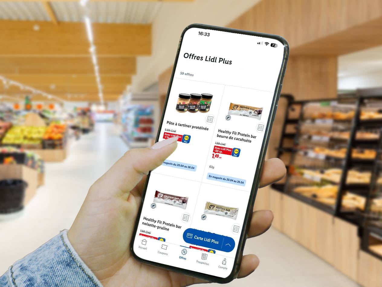 Main tenant un smartphone avec l'application Lidl Plus affichant des barres protéinées et de la pâte à tartiner protéinée dans un supermarché.