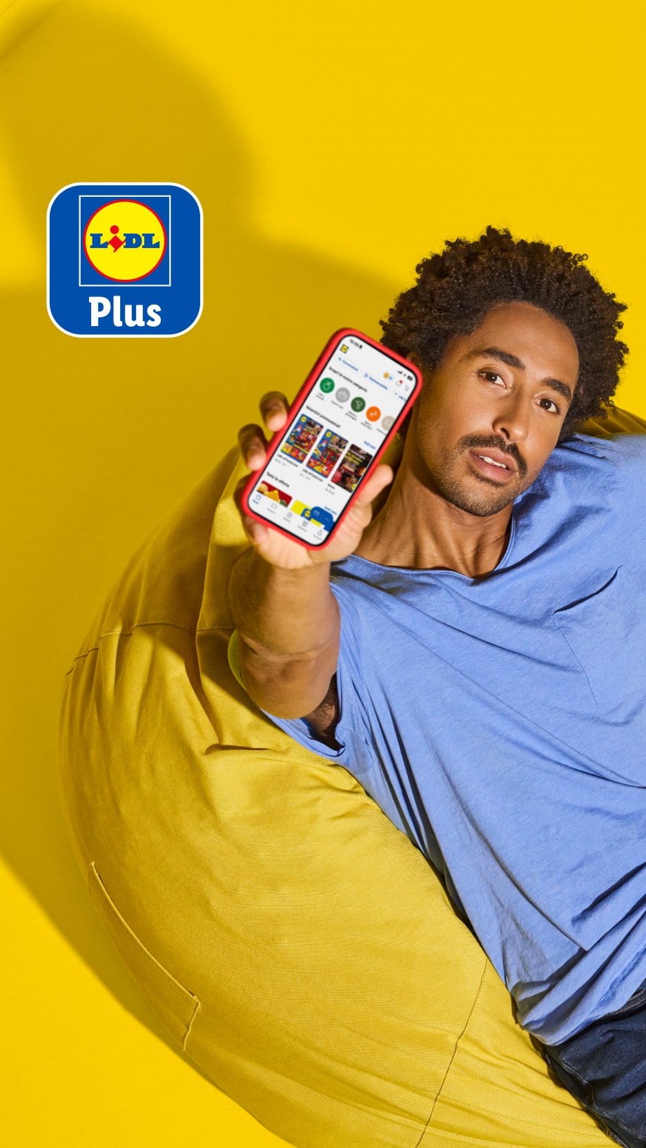 Lächelnder Mann zeigt App mit Angeboten für Lebensmittel und Haushaltsprodukte, mit Plus-Logo.