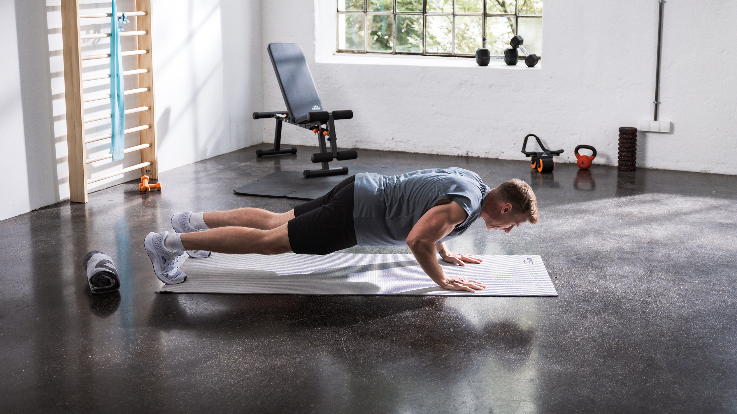 Homme faisant des pompes sur un tapis dans une salle de sport à domicile avec divers équipements de fitness.