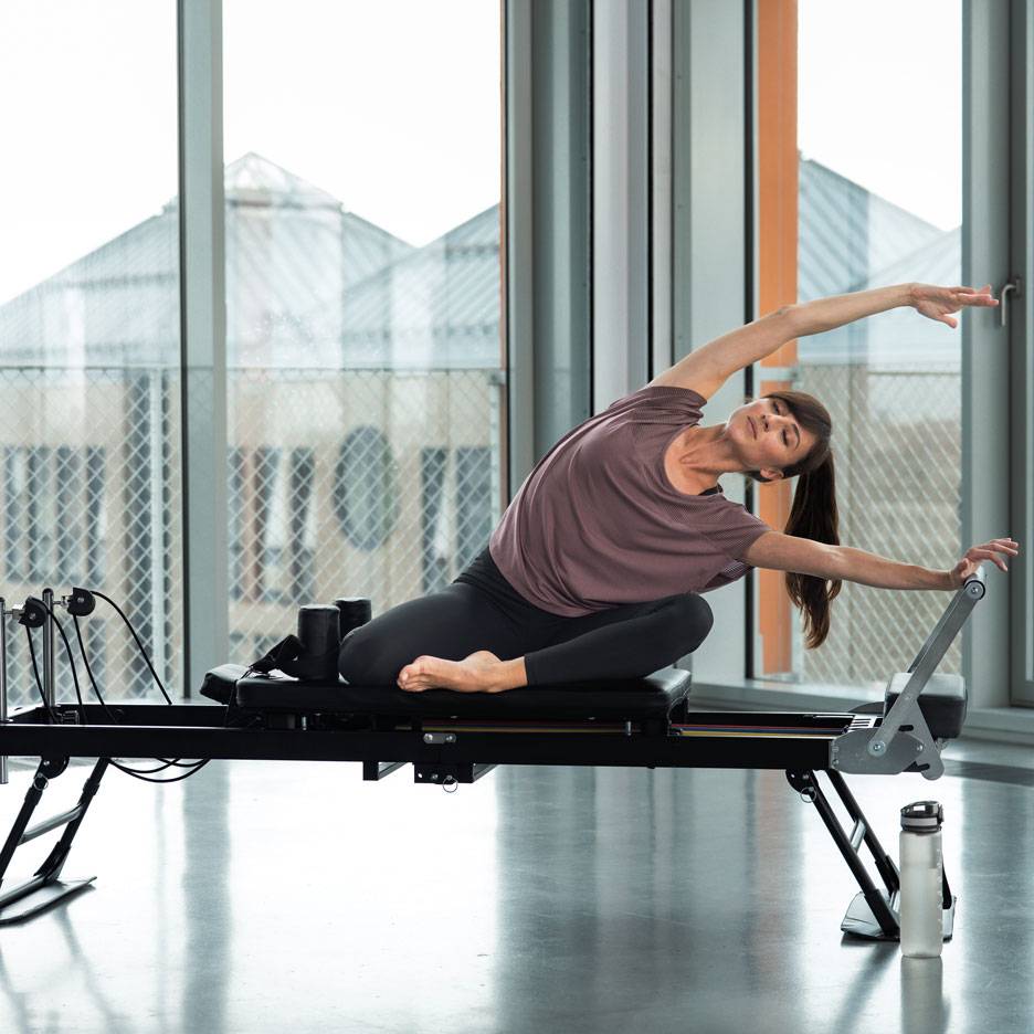 Donna che fa Pilates su una macchina reformer, allungandosi lateralmente.