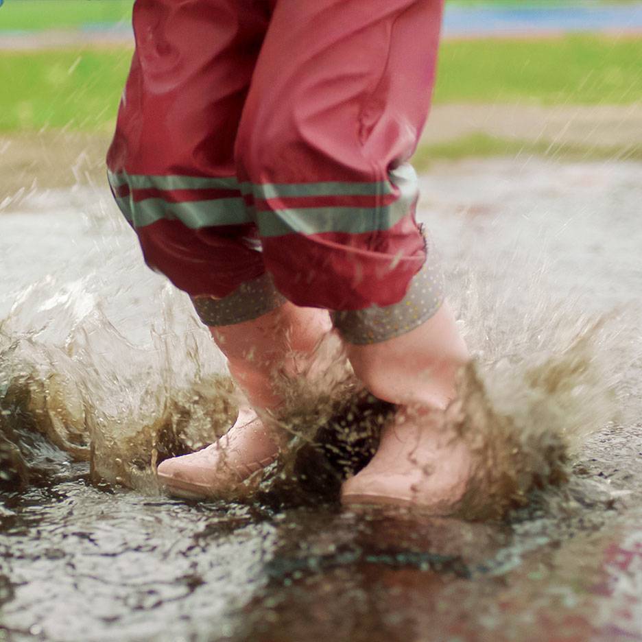 Enfant en pantalon imperméable rouge et bottes sautant dans une flaque.
