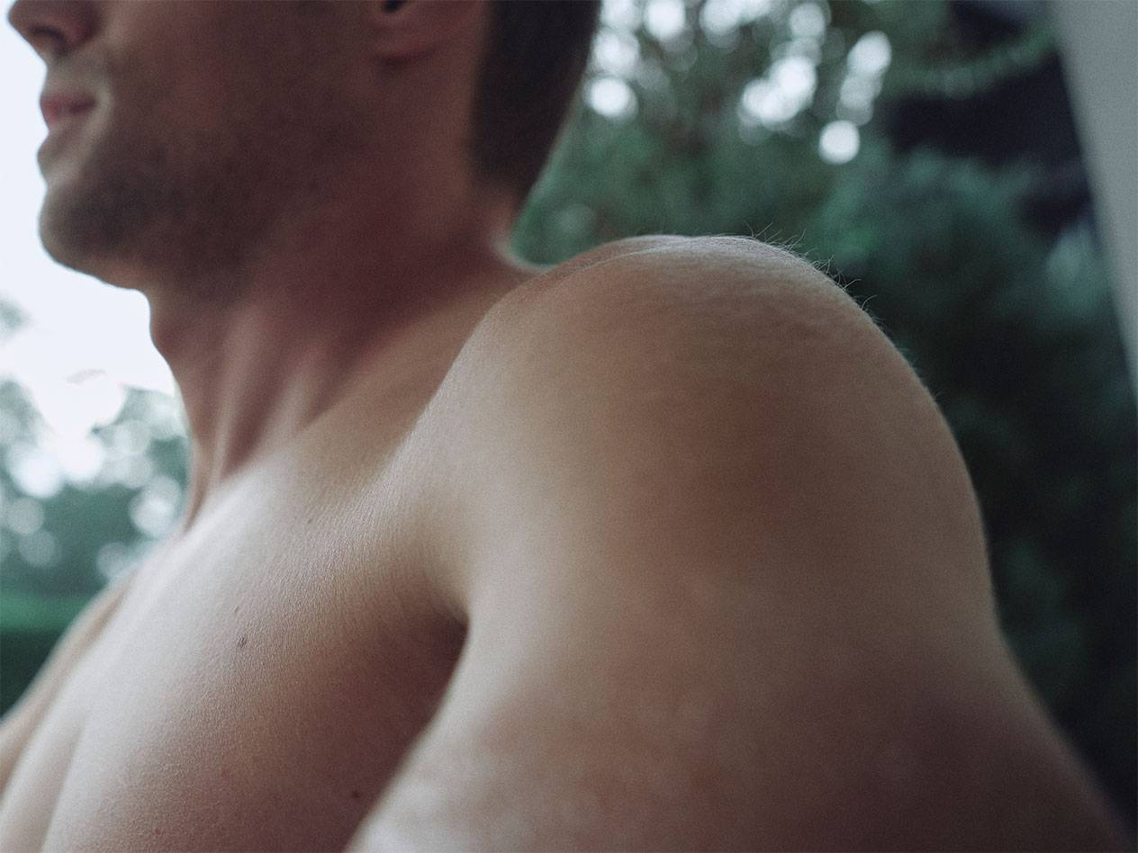 Primo piano della spalla e del collo di un uomo, con uno sfondo verde sfocato.