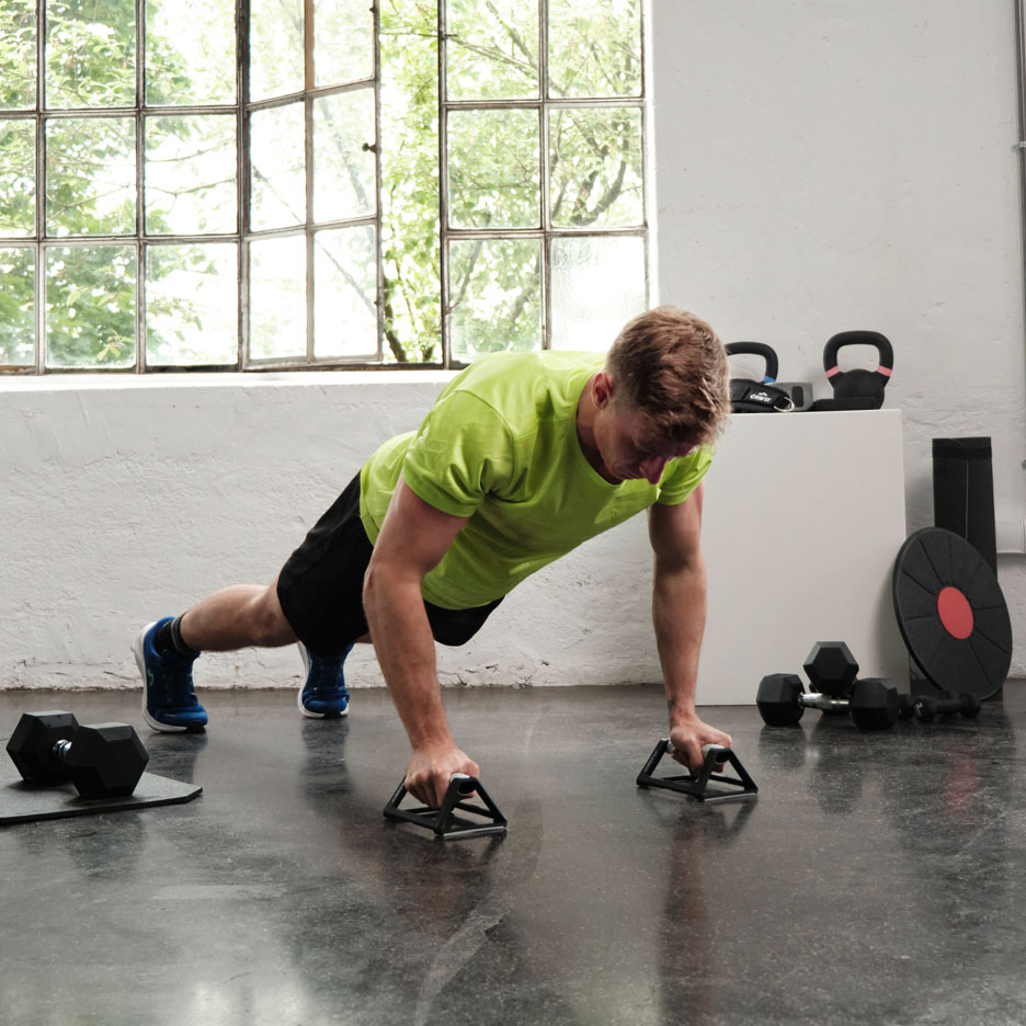 Homme faisant des pompes avec des poignées dans une salle de sport.