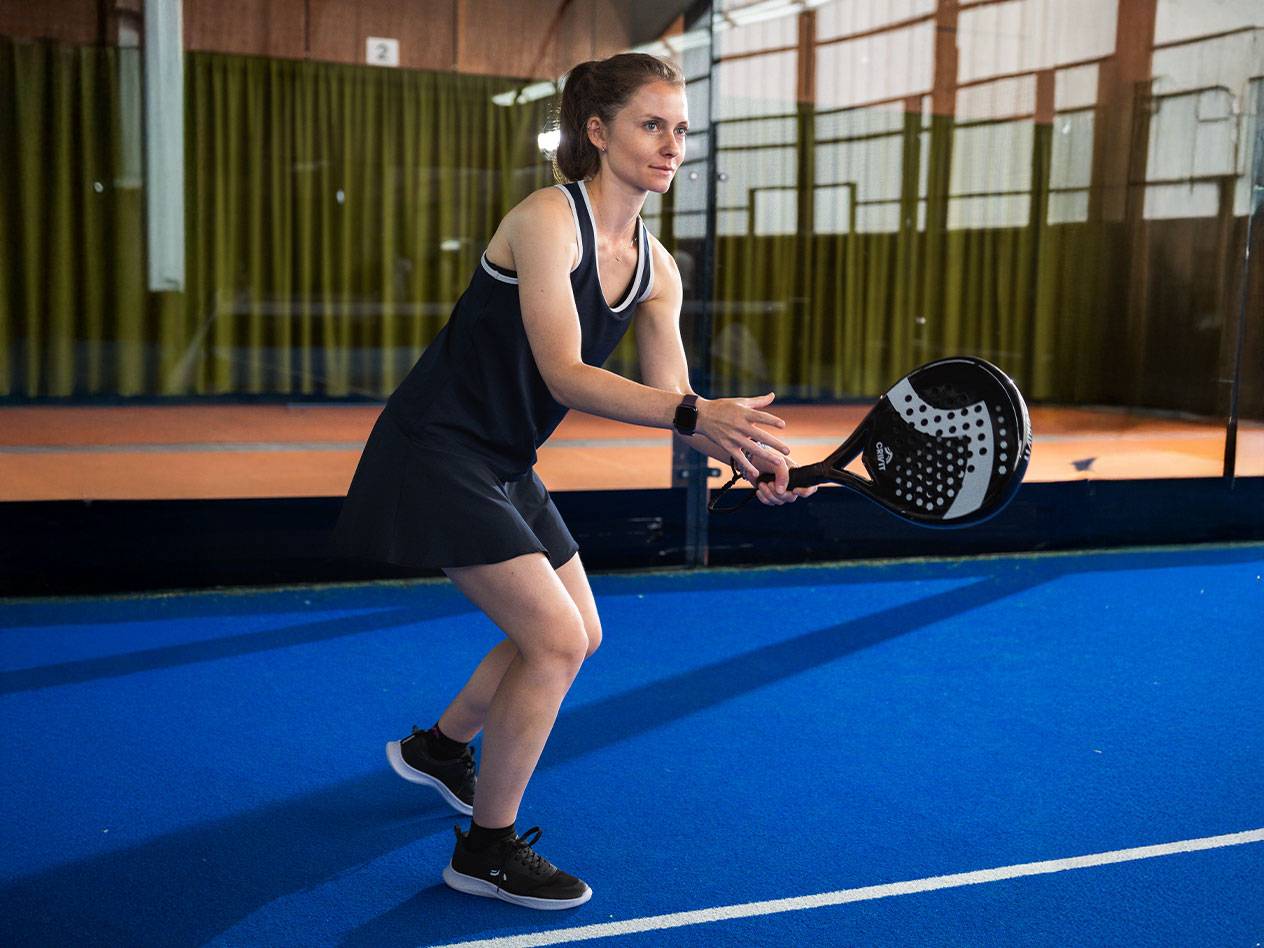 Donna in abito da padel nero con racchetta da padel nera su campo blu.