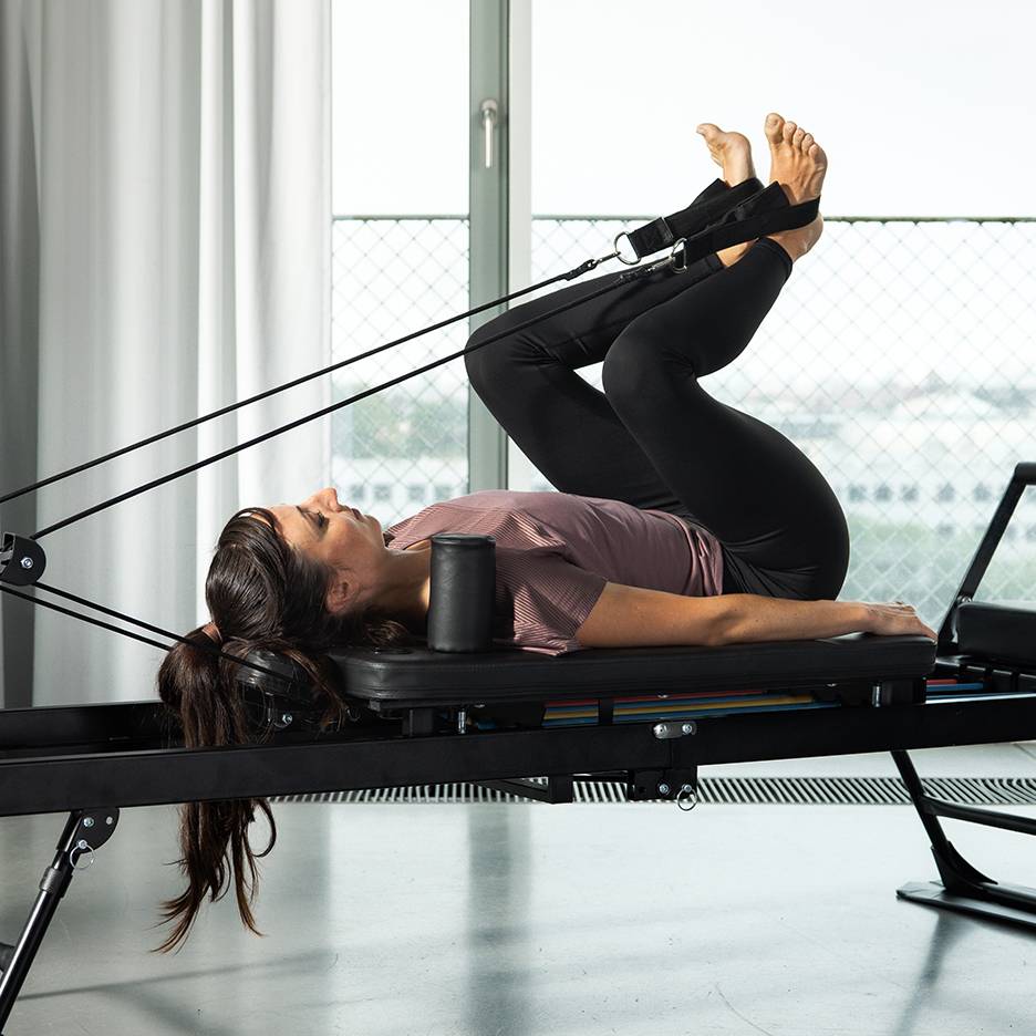 Donna che esercita le gambe su un reformer Pilates con fasce di resistenza.