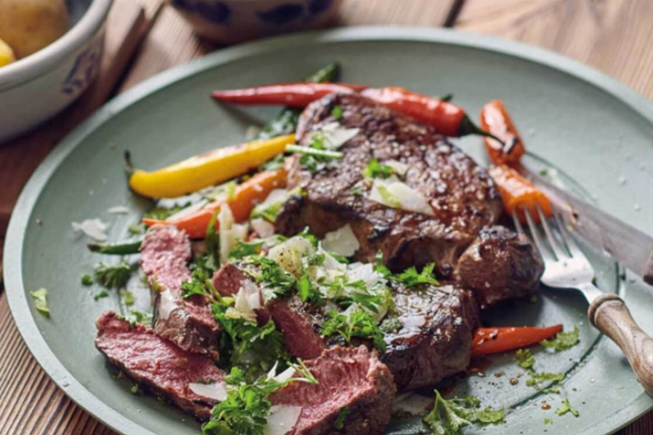 Gegrilltes Steak mit Paprika, frischen Kräutern und gehobeltem Käse auf einem grünen Teller.