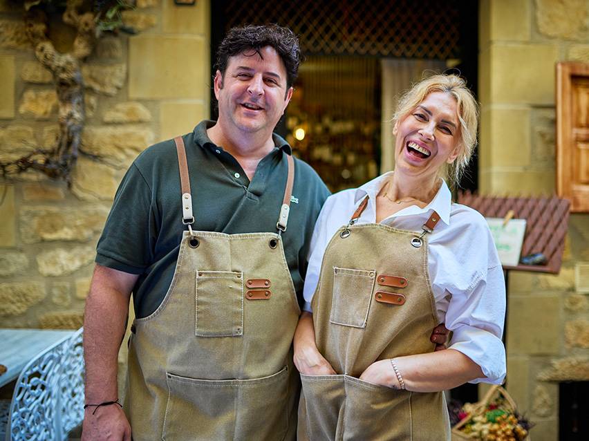 Homme et femme en tabliers de toile, souriant devant un magasin.