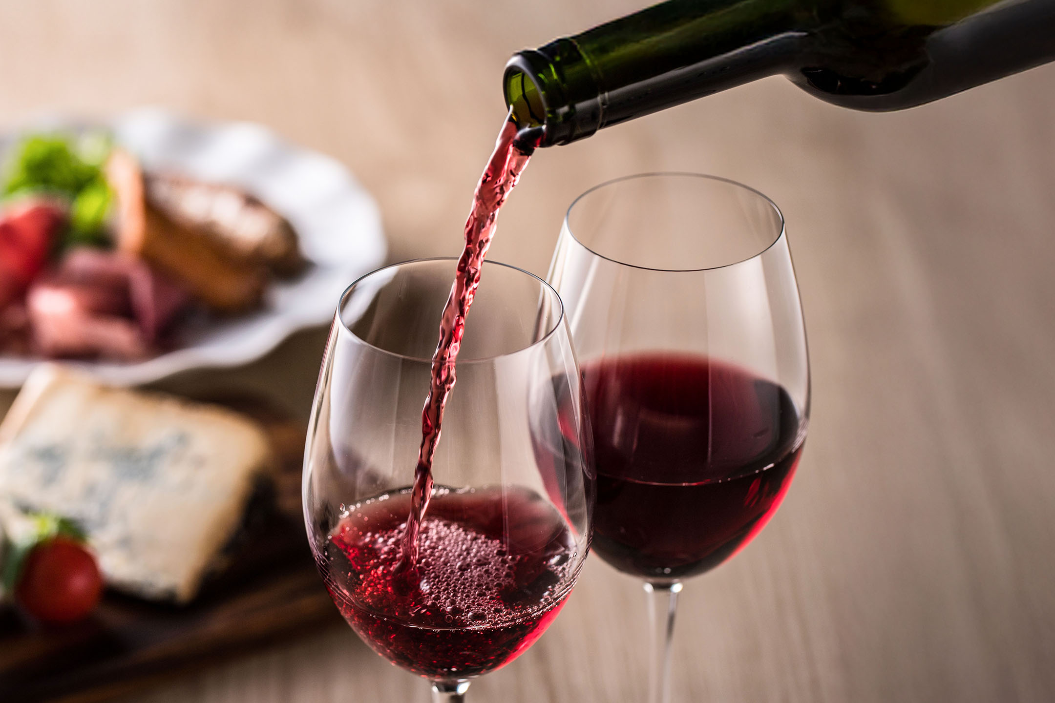 Rotwein wird in ein Glas gegossen, mit Vorspeisen im Hintergrund.