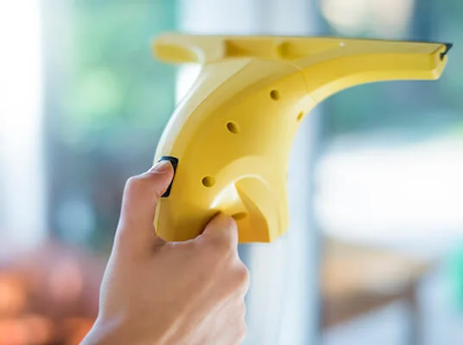 Mano che tiene un lavavetri elettrico giallo, pulendo una finestra.