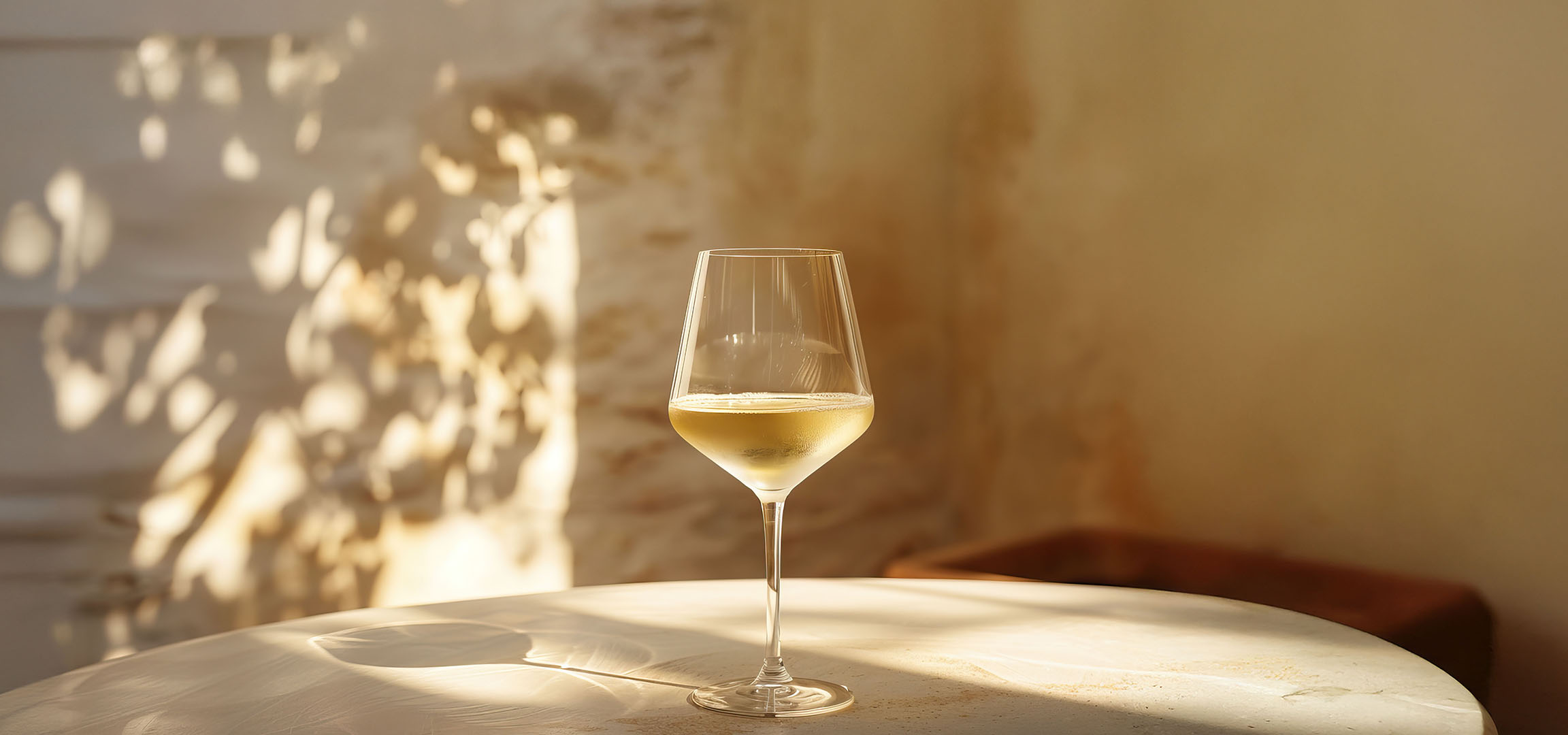 Verre de vin blanc sur une table, avec des ombres de feuilles et de colonnes.
