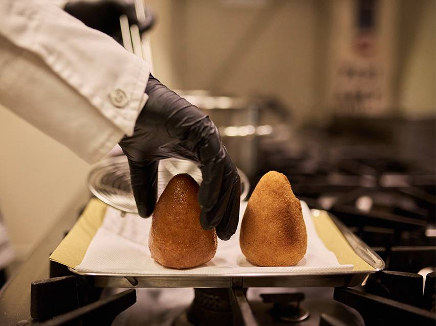 Chef en gants noirs plaçant des arancini frits sur un plateau avec des serviettes en papier.