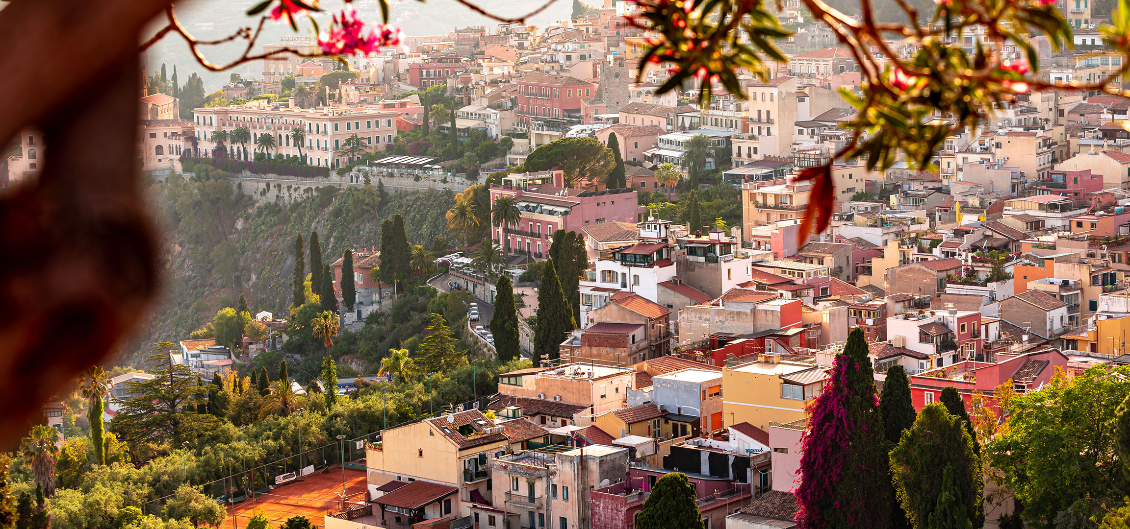 Vue panoramique sur une ville méditerranéenne avec des bâtiments colorés et de la verdure.